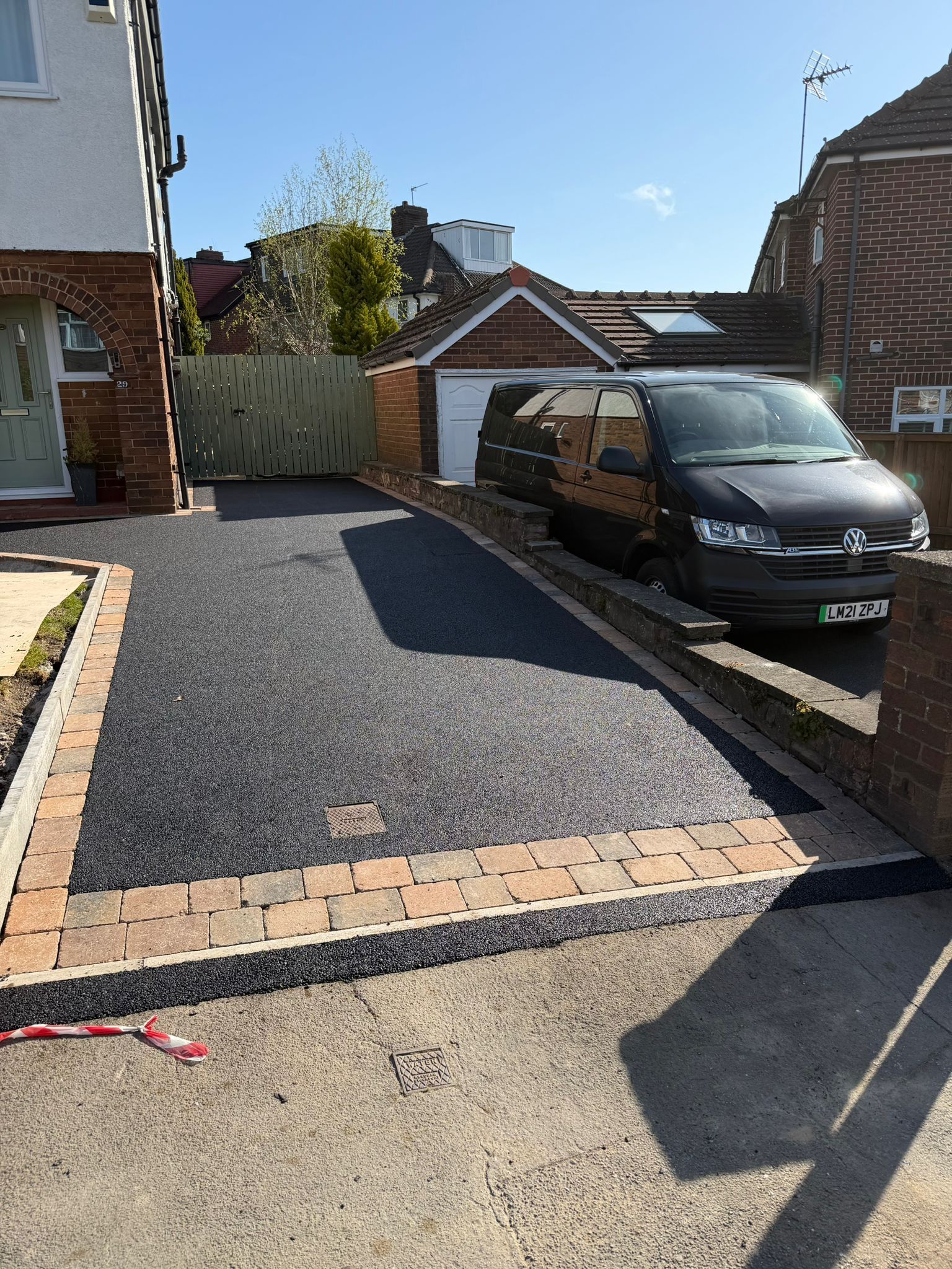 Driveway with fresh black gravel, a parked black van, and brick houses on a sunny day.