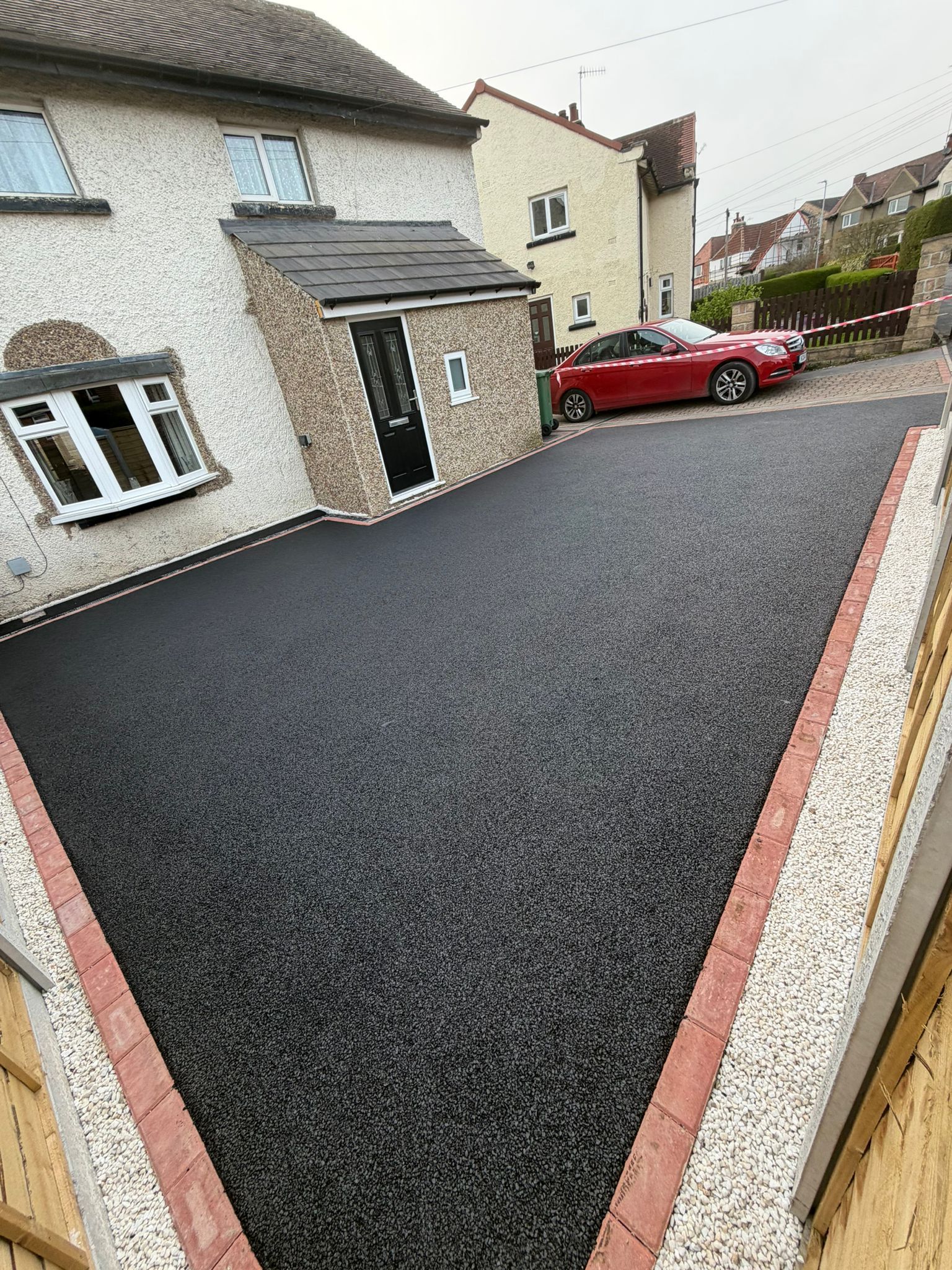 Freshly paved black driveway beside a stone house, with a red car parked nearby.