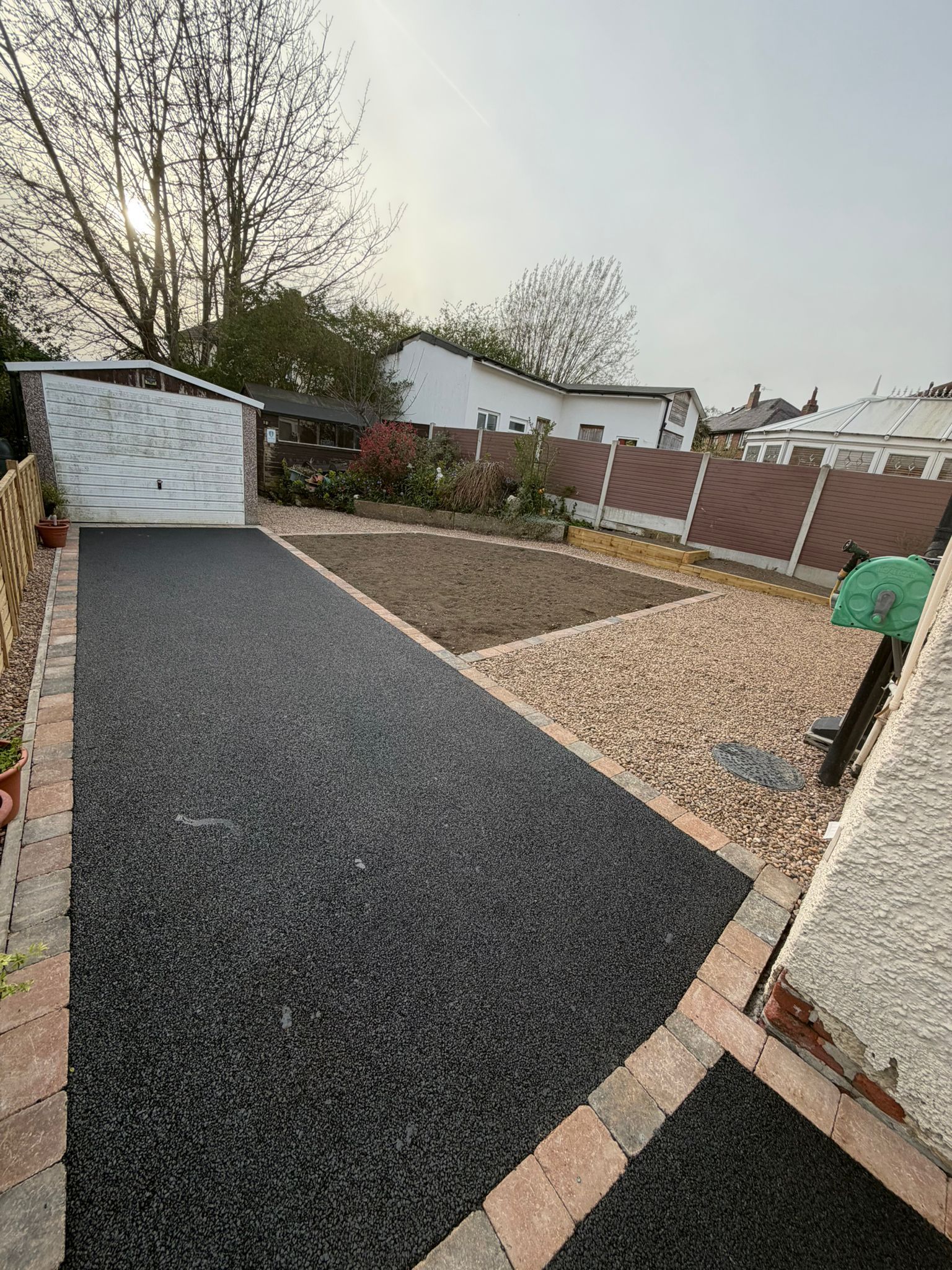 Gravel backyard path beside a shed and fence, with a planted bed and patio edging.