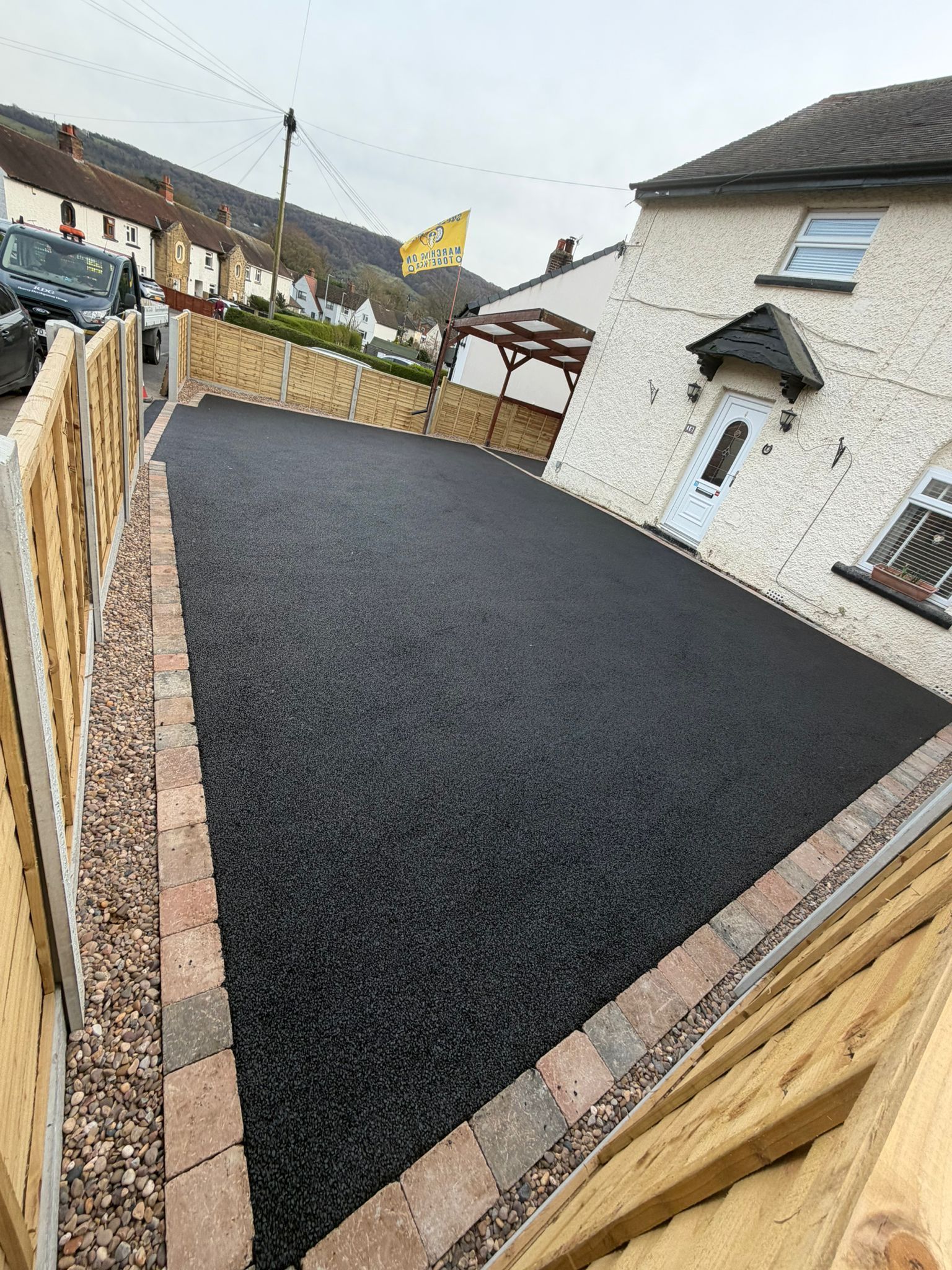 Freshly paved black driveway beside a white house and wooden fence in a residential yard