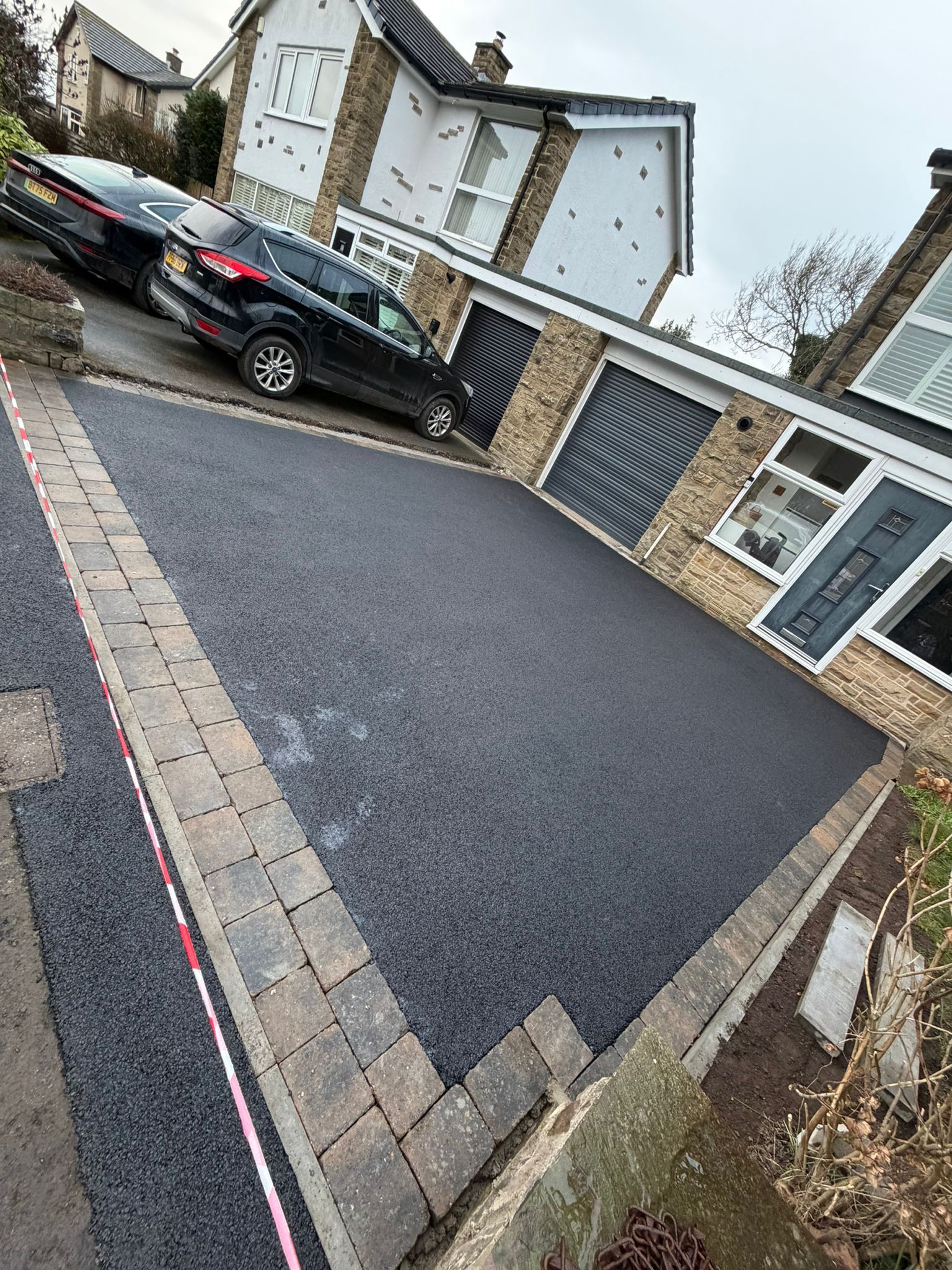 Freshly paved driveway beside a brick wall with a black car parked on the left