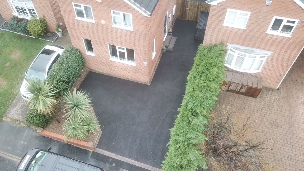 Aerial view of a brick apartment building with parking spaces, hedges, and a paved driveway
