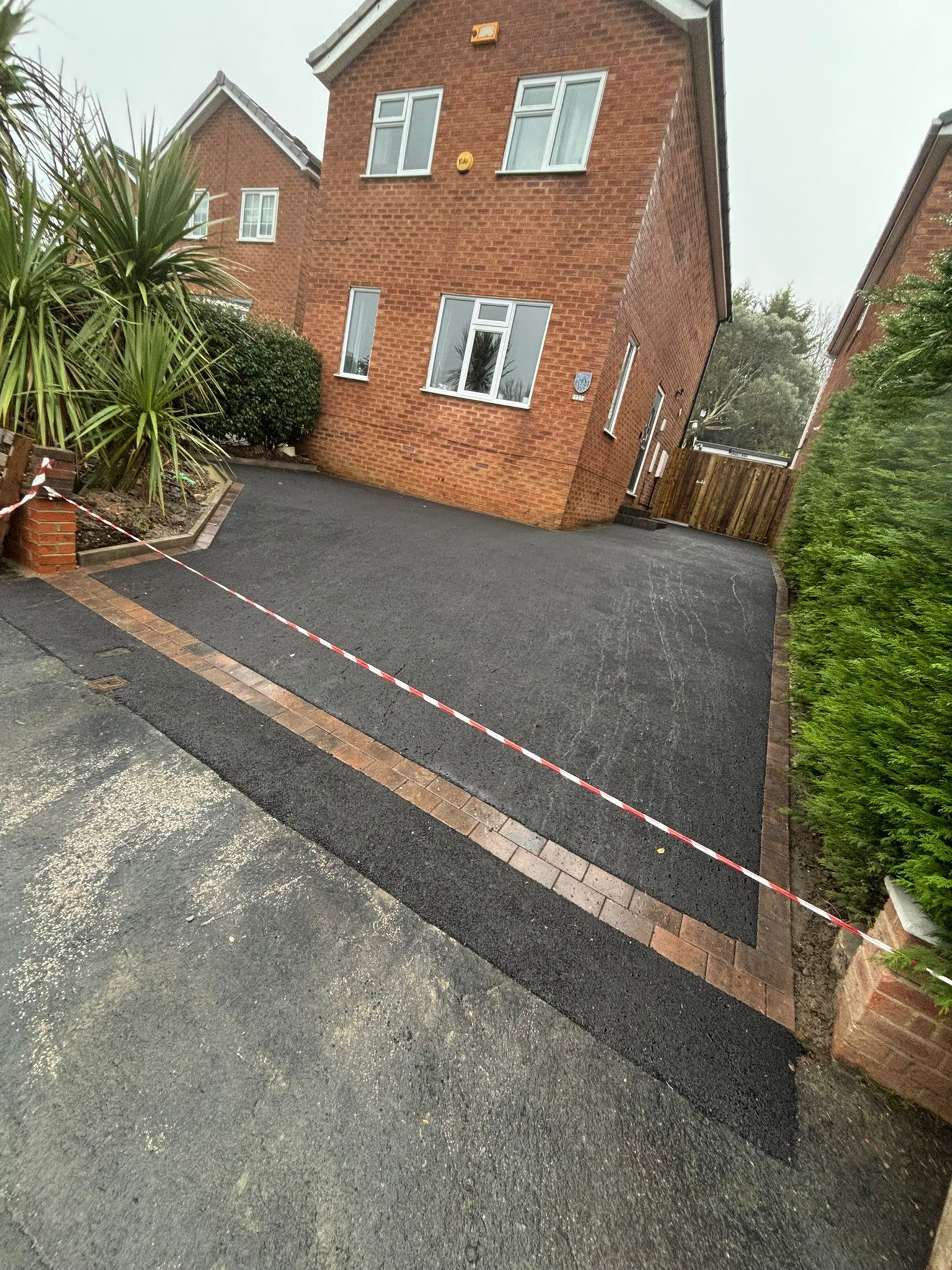 Brick house with gravel driveway blocked by red-and-white tape and bordered by hedges