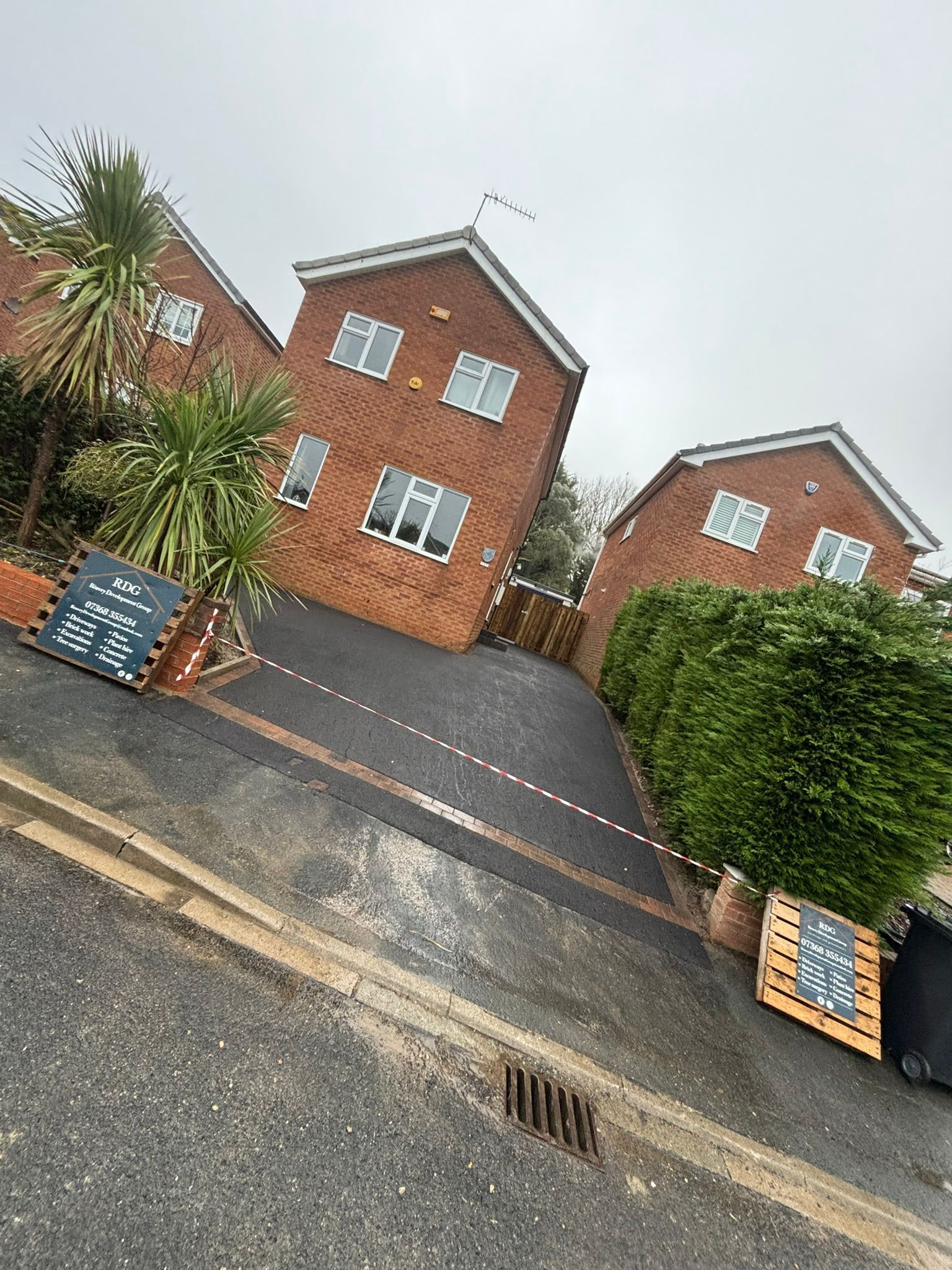 Row of red-brick townhouses with driveways, seen from a tilted street view on a cloudy day
