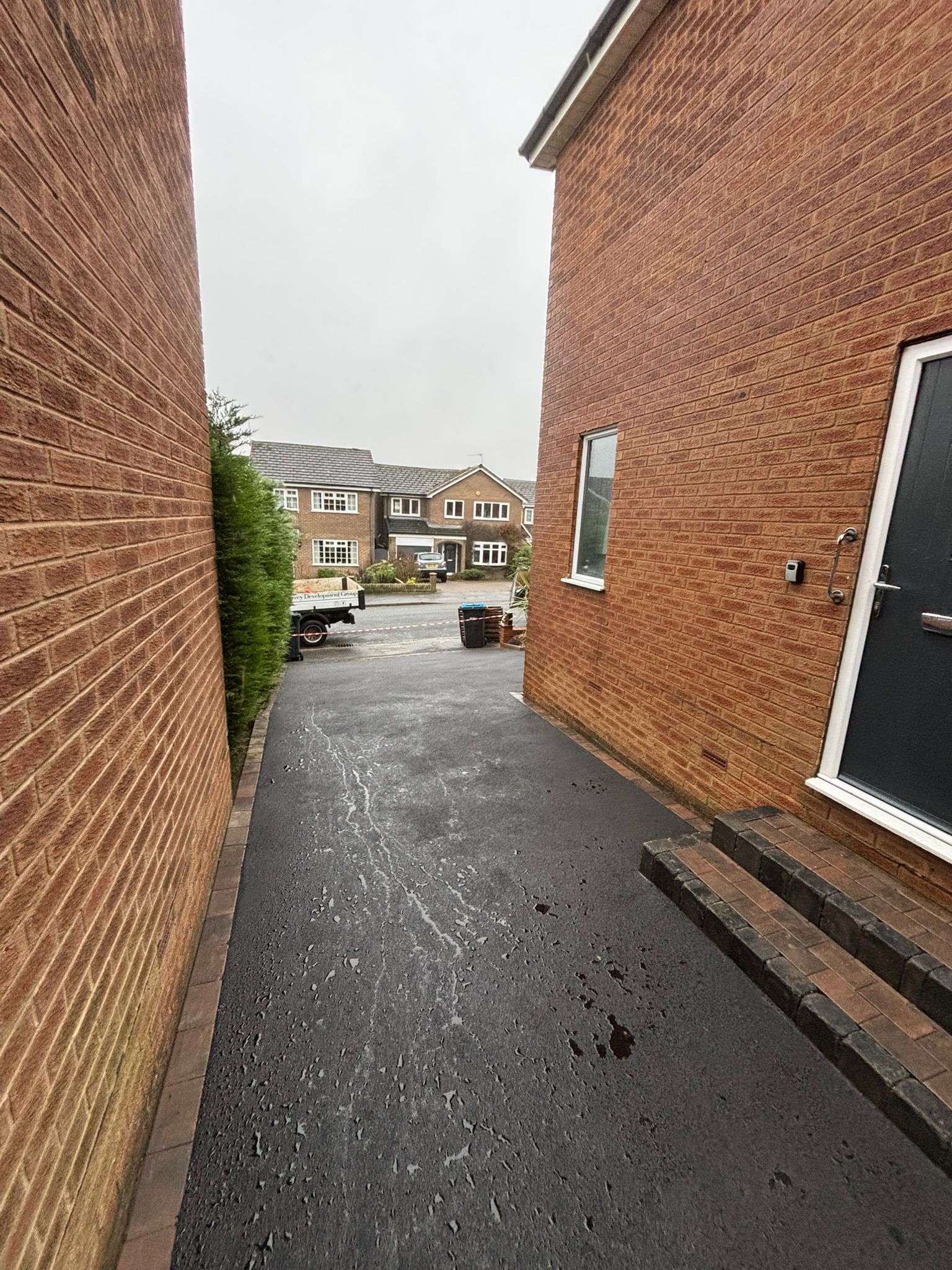 Narrow wet alley between red brick houses, leading to a residential street with parked cars.