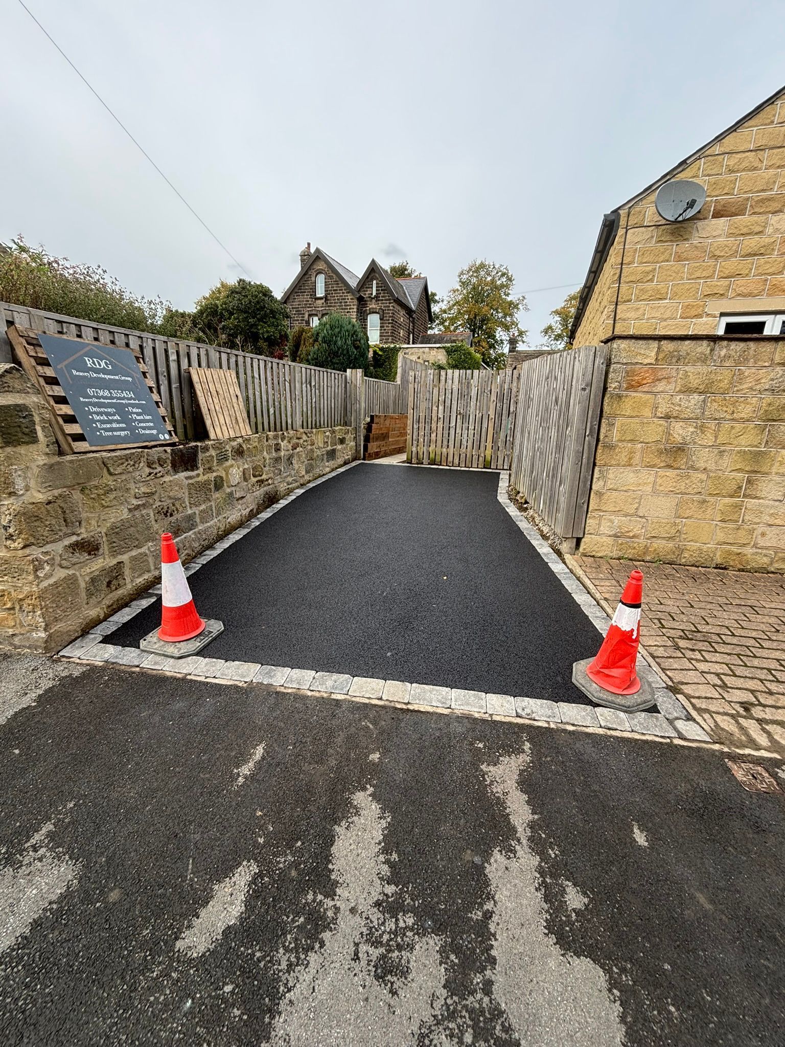 Narrow stone path between walls with orange cones, leading to a building in the distance