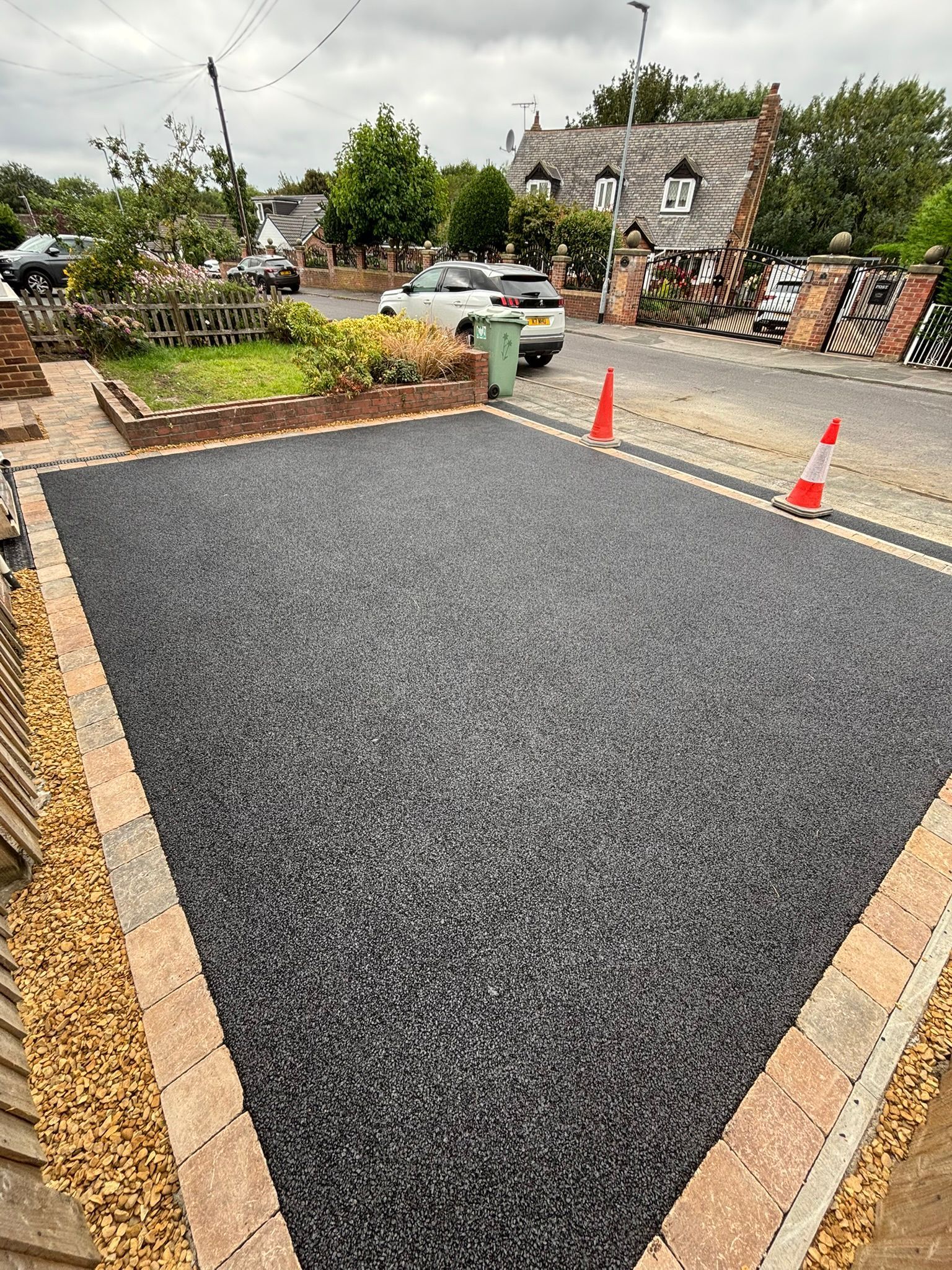 New gravel driveway bordered by brick edging and orange cones in a suburban front yard
