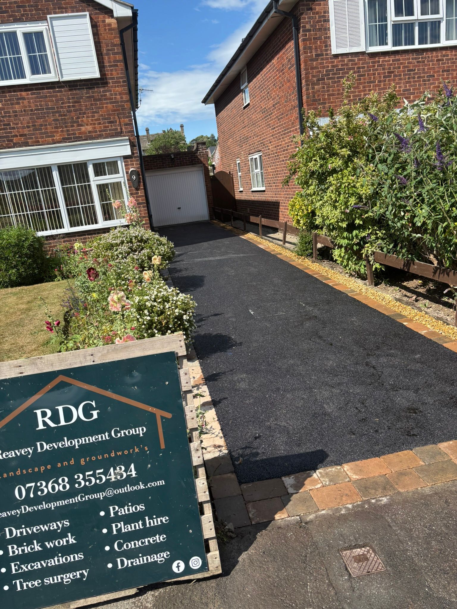 New black gravel driveway between two red-brick houses, with RDG Landscaping sign in foreground.