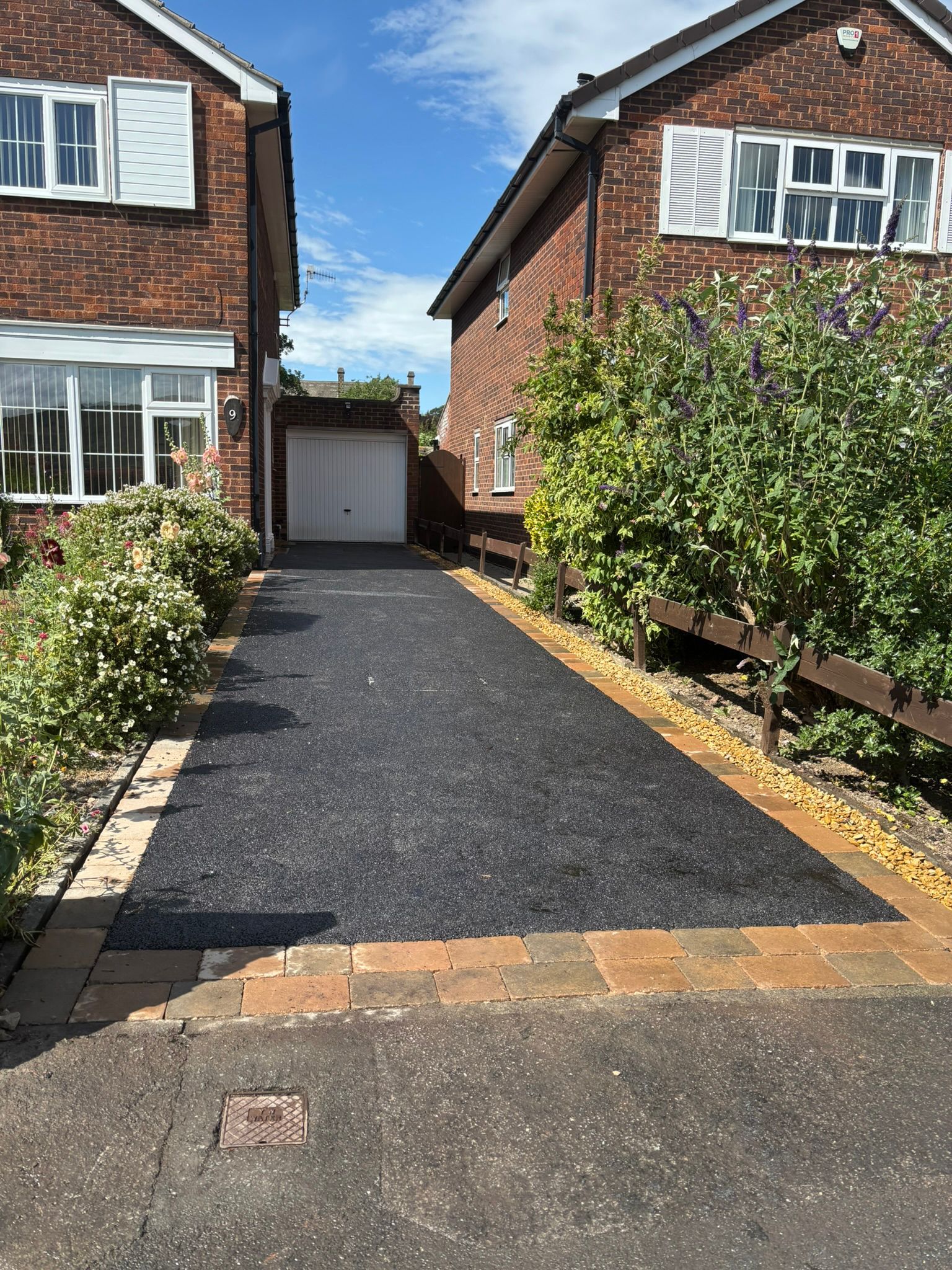 Driveway between two brick houses leading to a garage, with gravel and a small front garden.