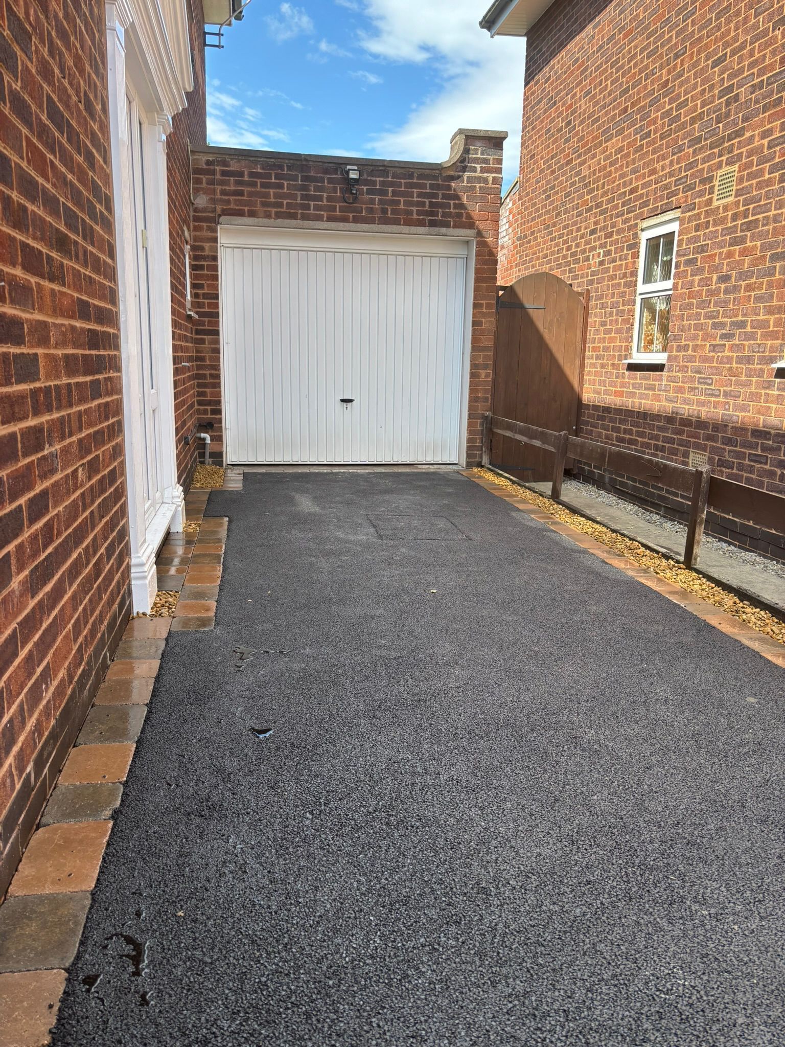 Narrow gravel driveway between brick houses leading to a white garage door