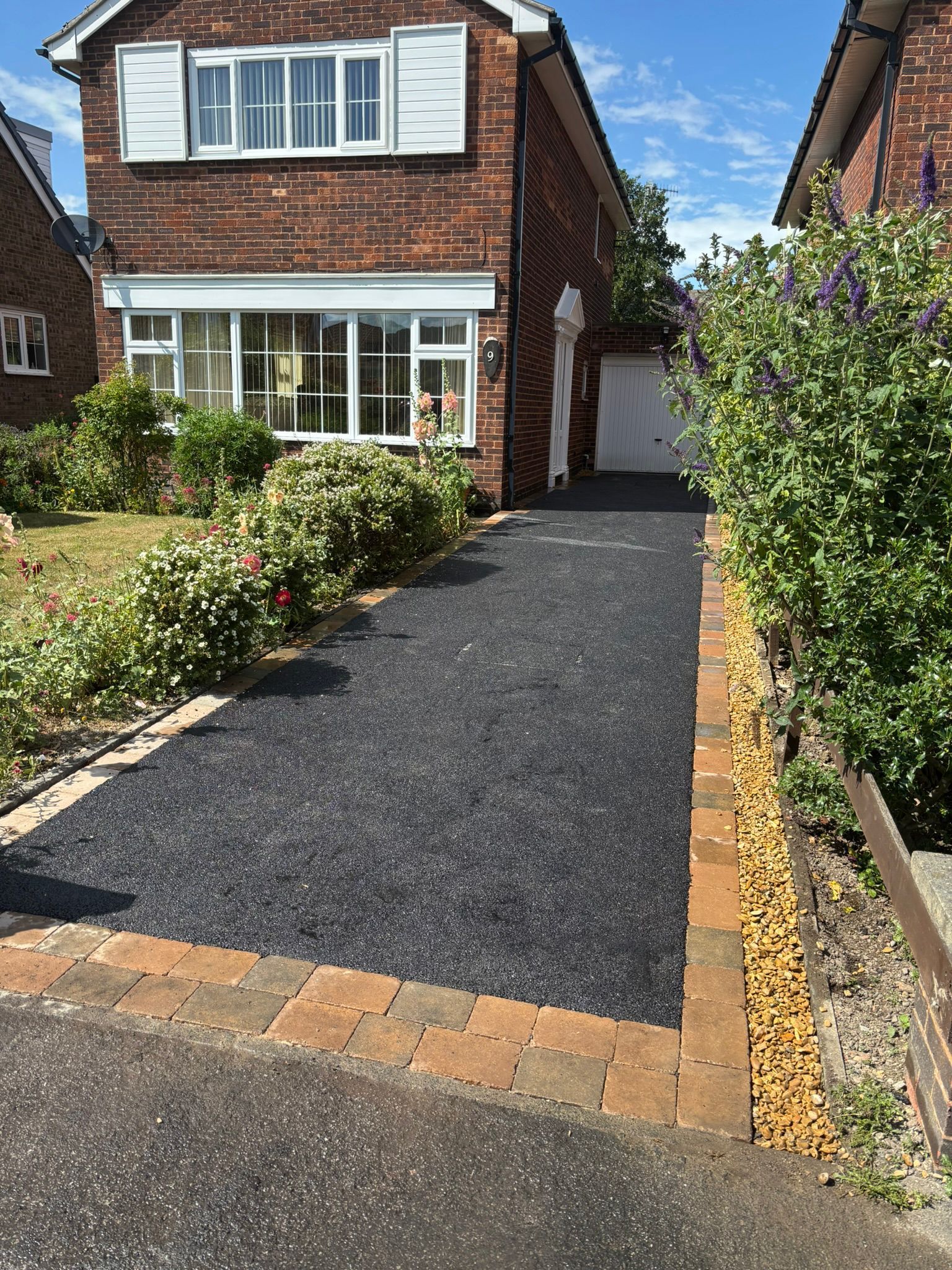 Brick house with a new black gravel driveway, bordered by flowers and brick edging