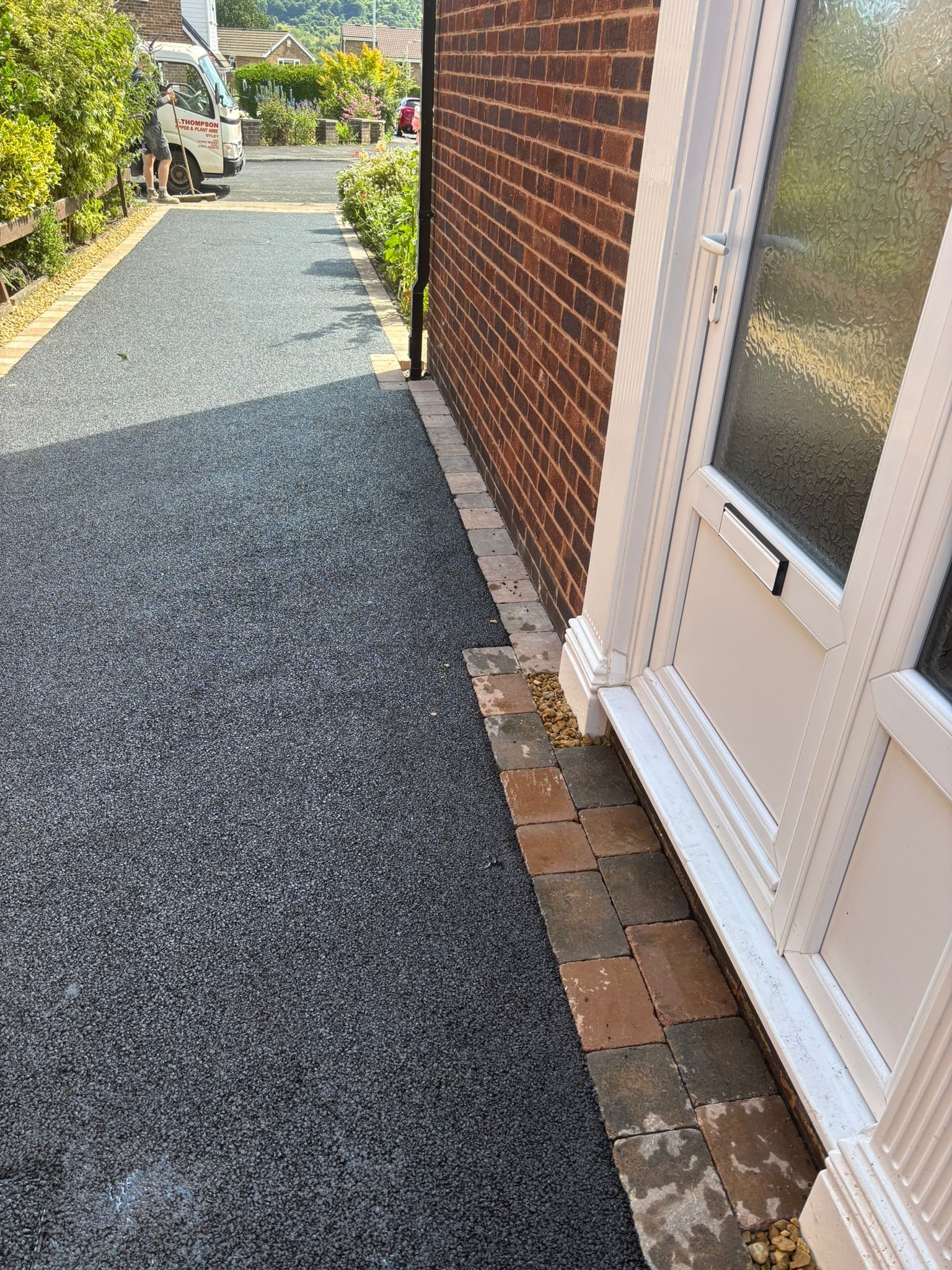 Narrow gravel side path beside a brick house and white door, leading to a garden gate.
