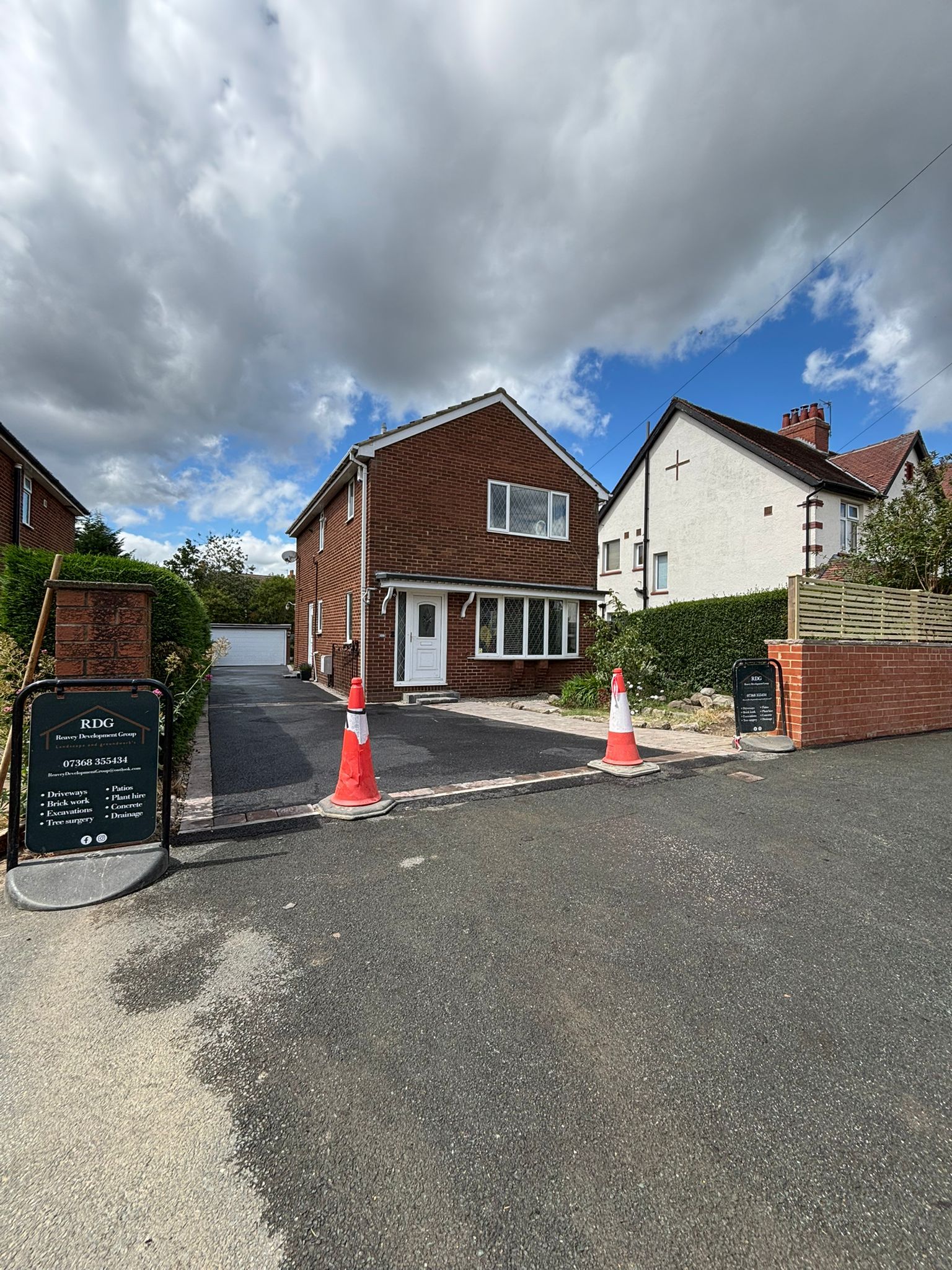 Newly built brick house with gravel driveway, traffic cones, and cloudy sky