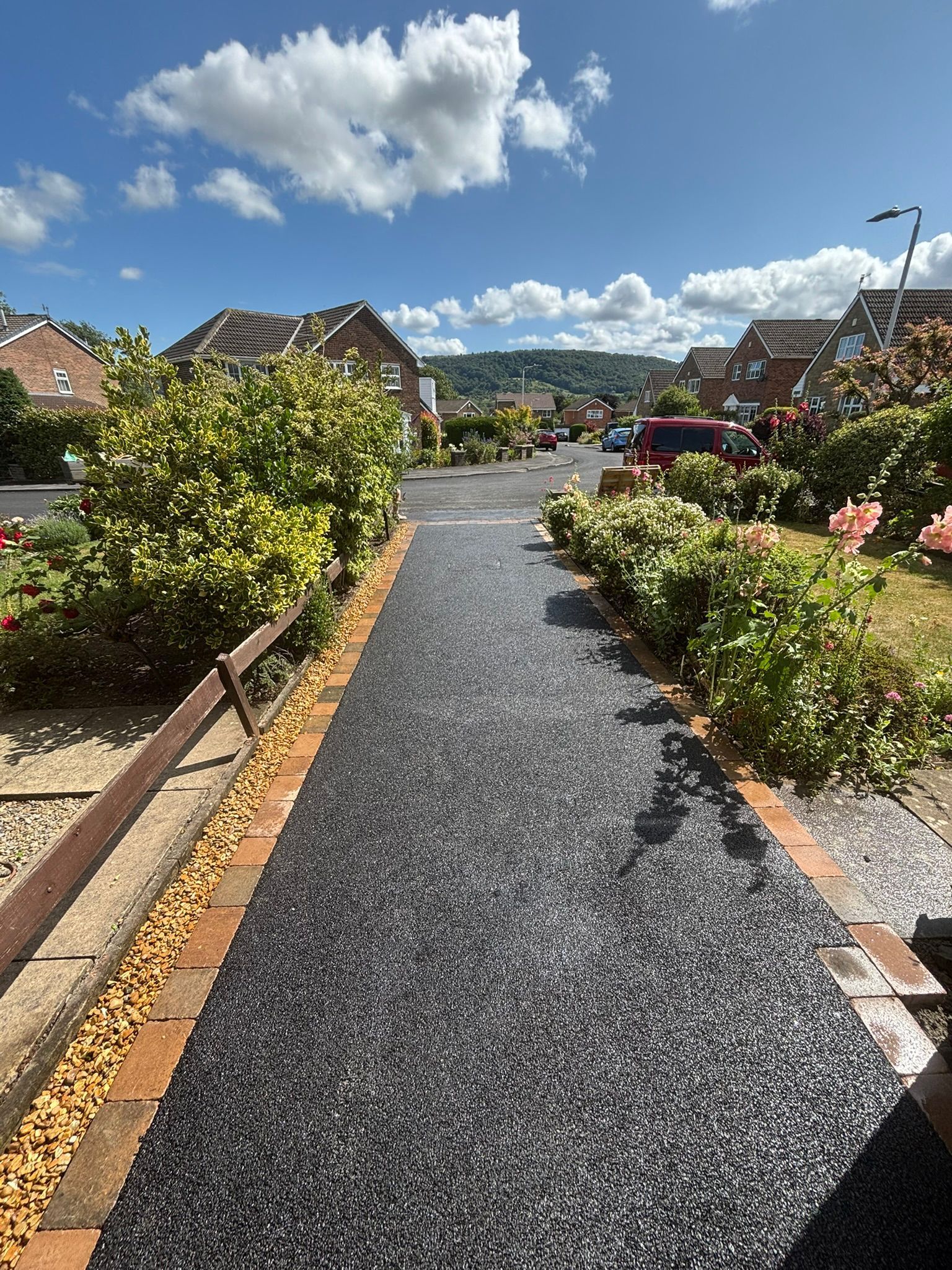 Gravel path through flower-lined houses under a bright blue sky with clouds