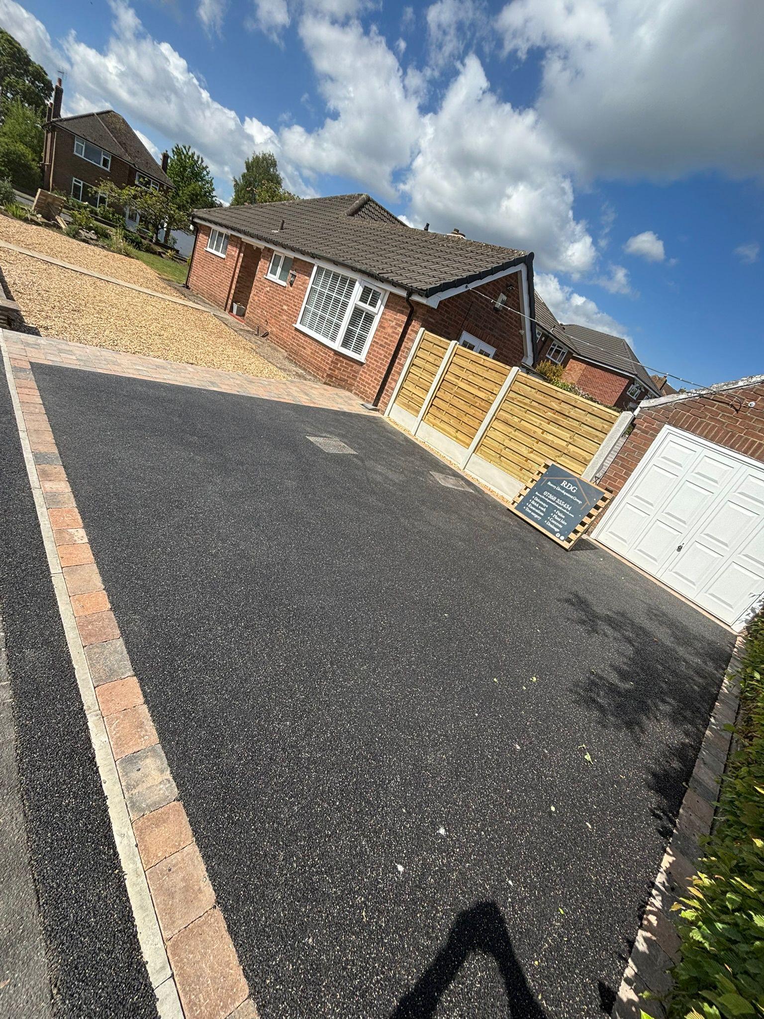 Newly paved black driveway beside a brick house under a blue, cloudy sky