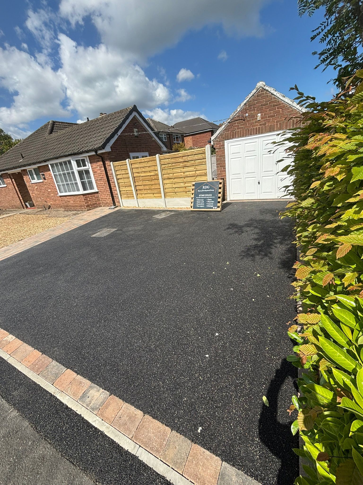 Suburban brick house with a new black driveway, garage door, and a sign by the entrance.