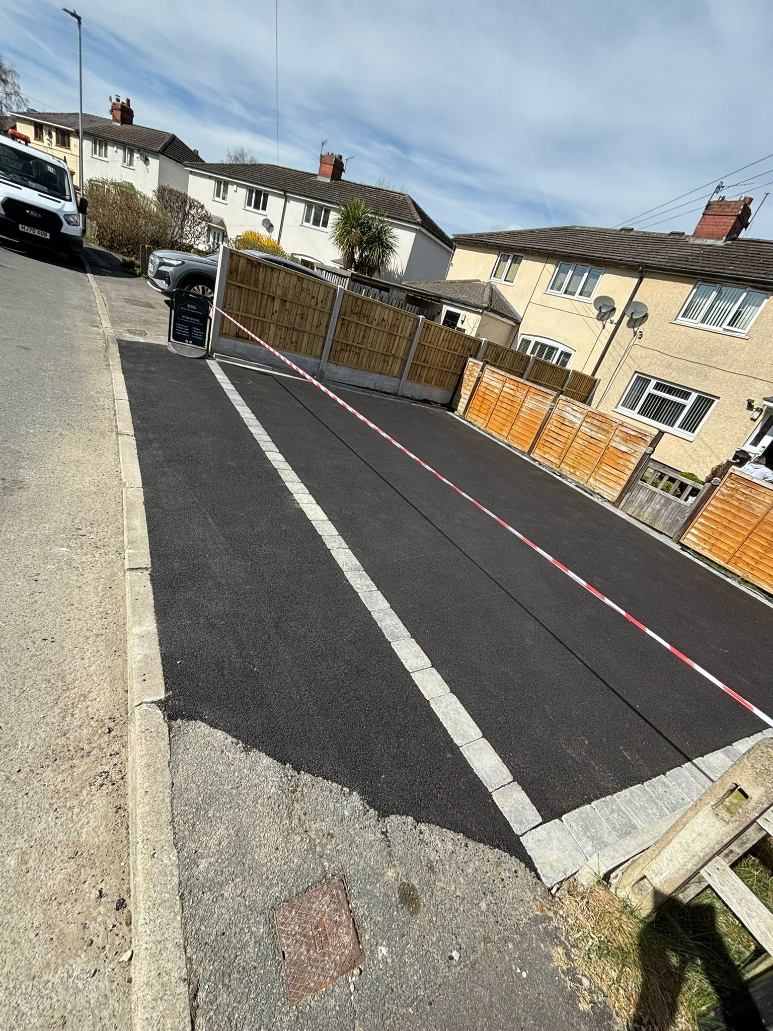 Worker painting a road marking on a residential street beside houses and fences.