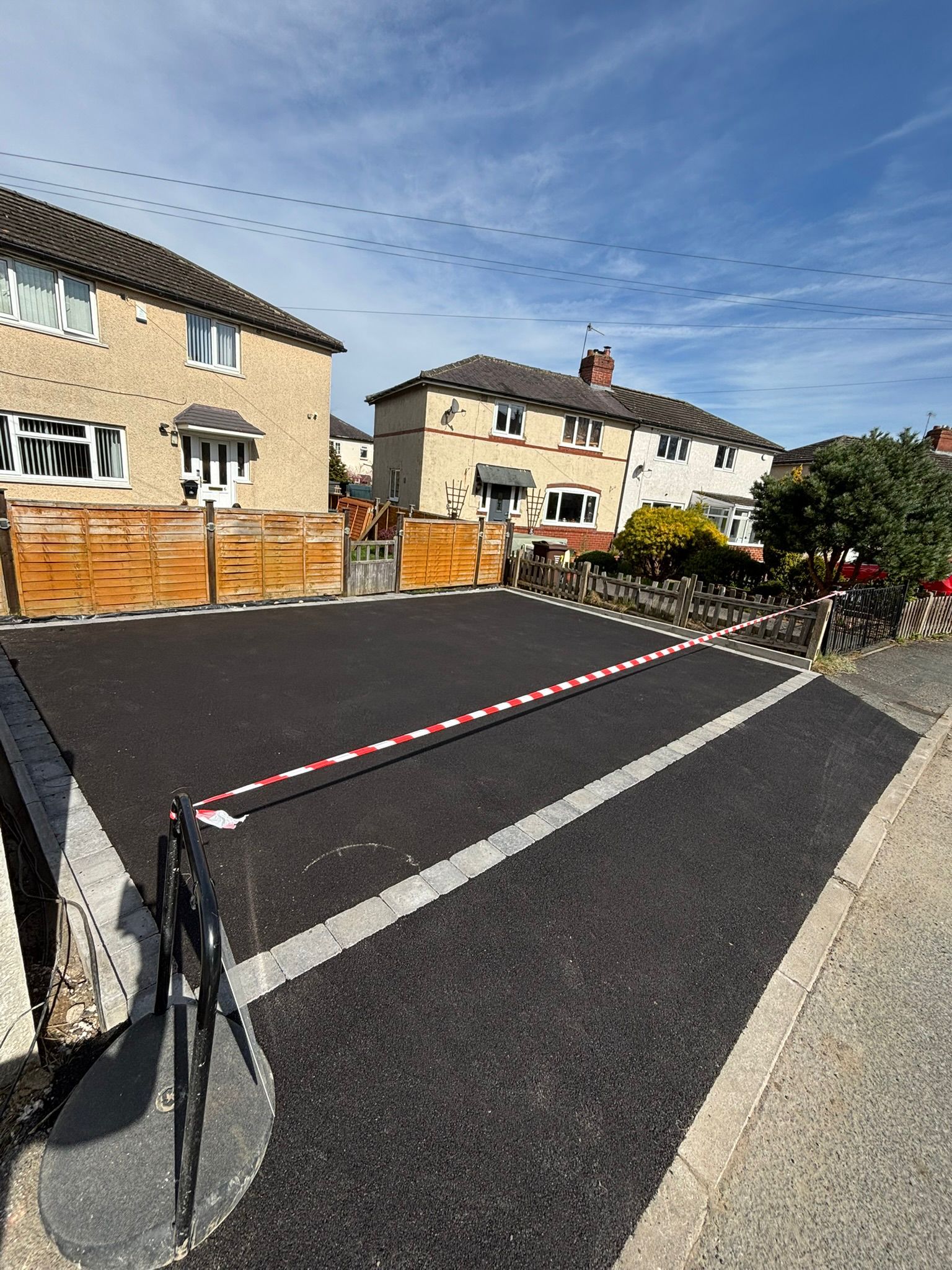 Residential street blocked by red-and-white barrier tape under a blue sky
