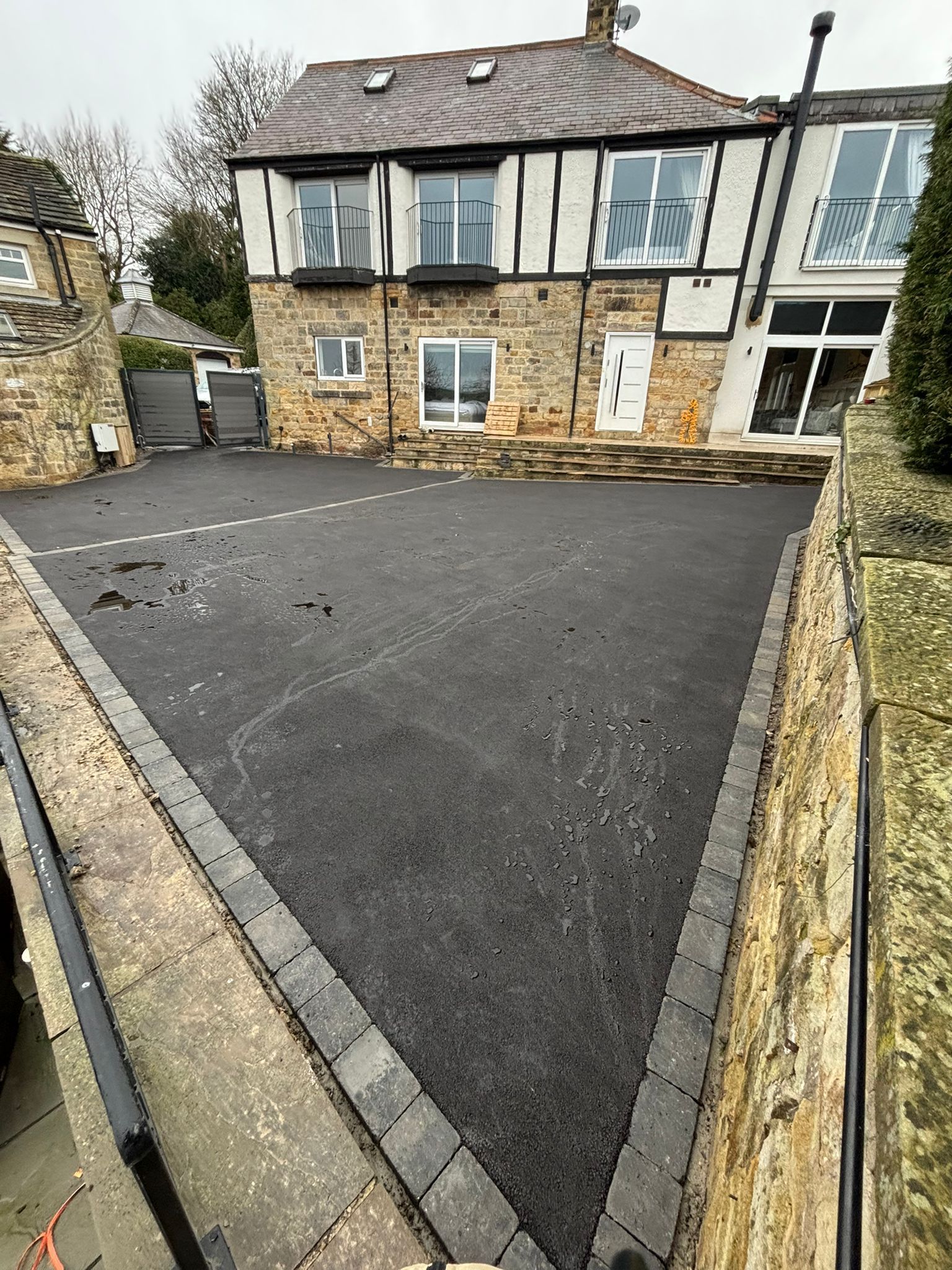 Stone house with dark asphalt driveway and a low stone wall on a cloudy day