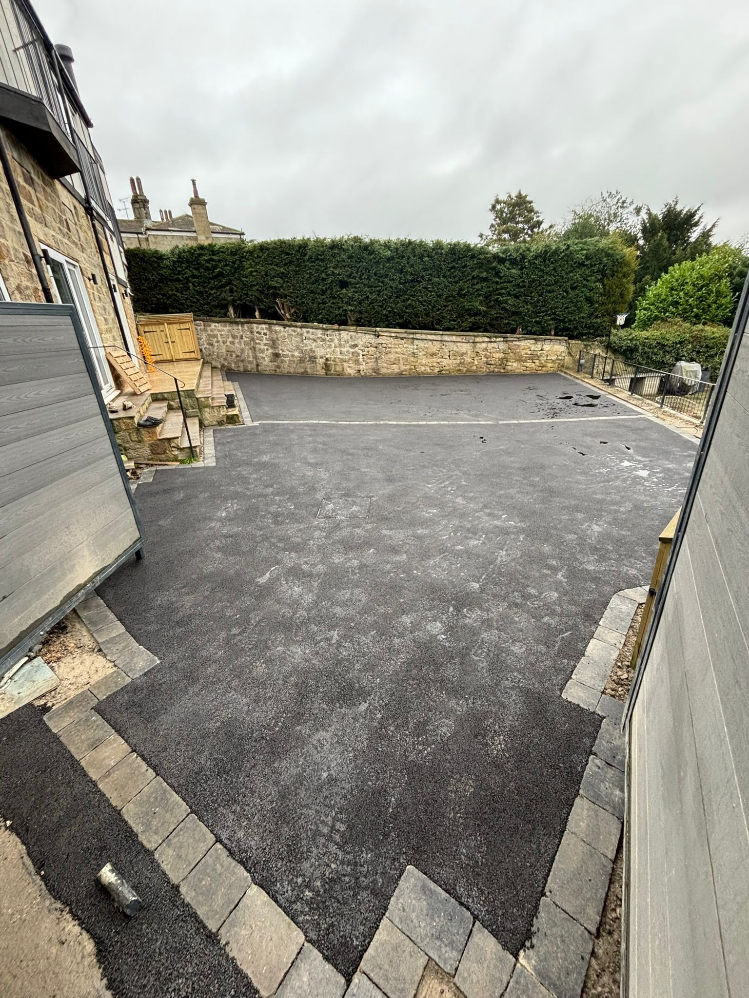 Empty paved driveway between stone walls and hedges on a cloudy day