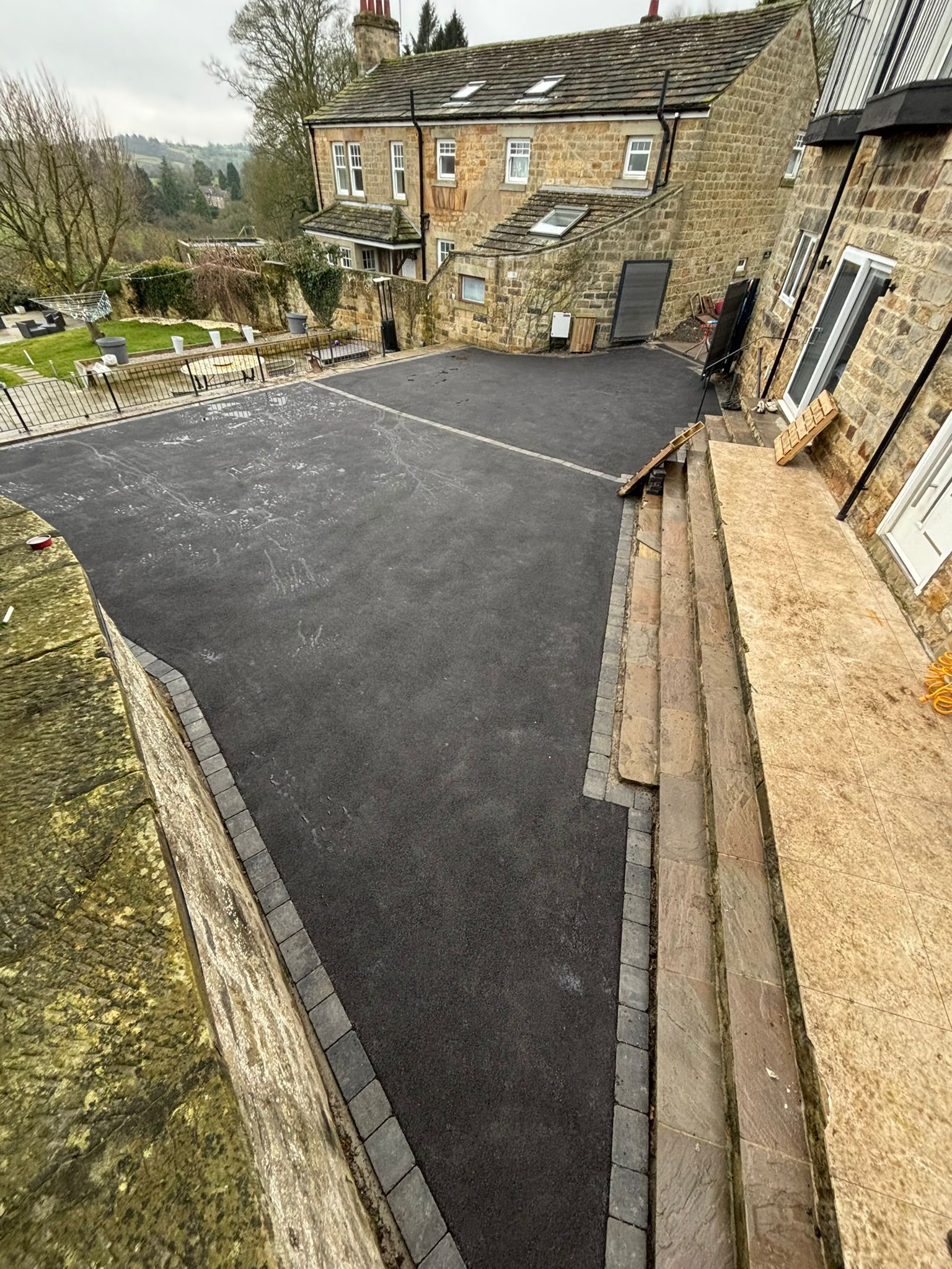 Stone courtyard with fresh black asphalt paving beside an old stone house and steps
