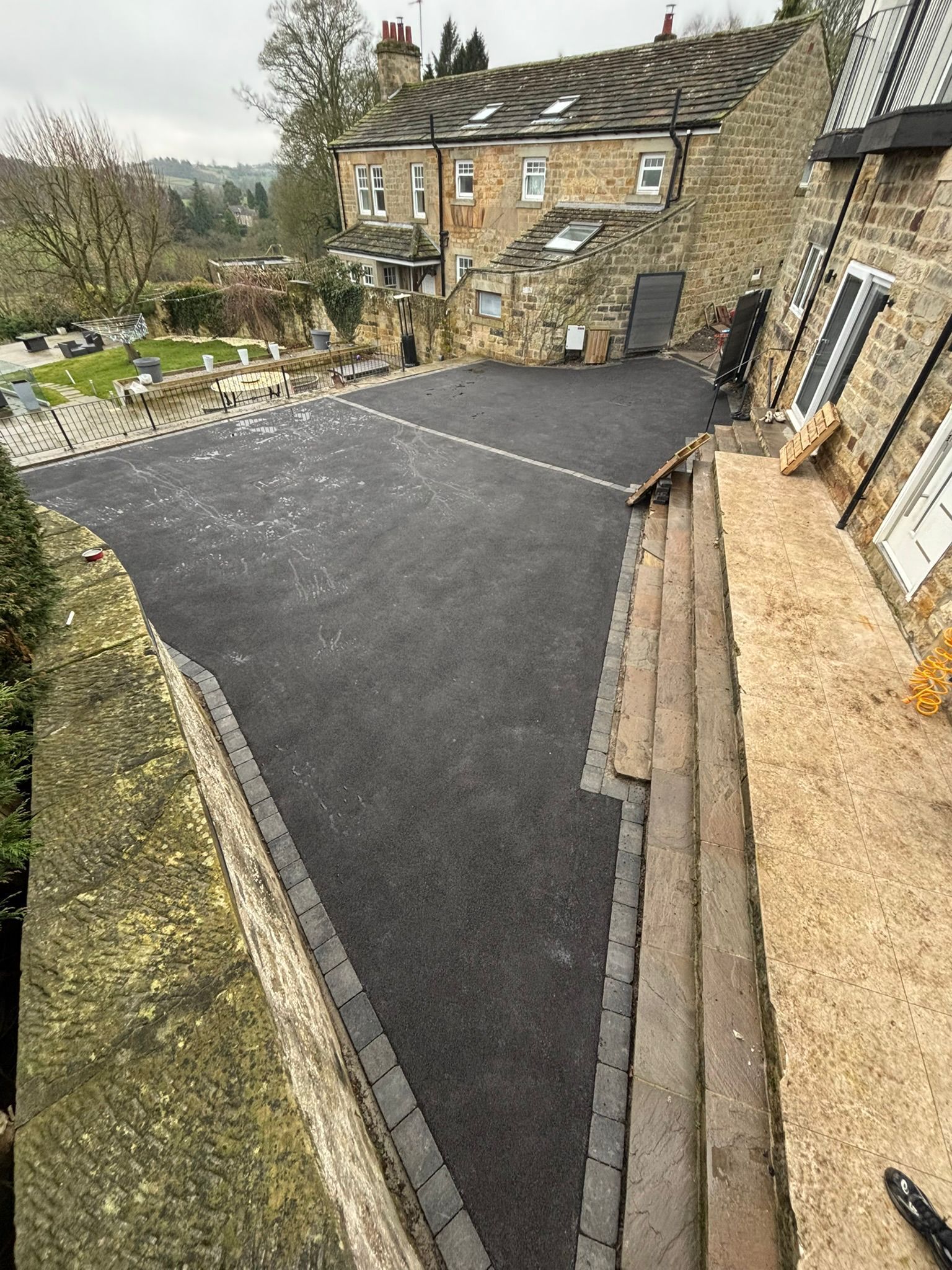 Stone house courtyard with fresh black paved driveway and steps beside a sloped garden.