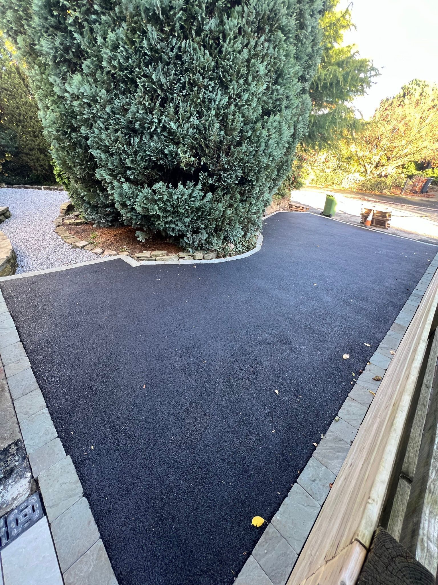 Freshly laid black gravel path beside a large evergreen shrub and wooden fence in a garden