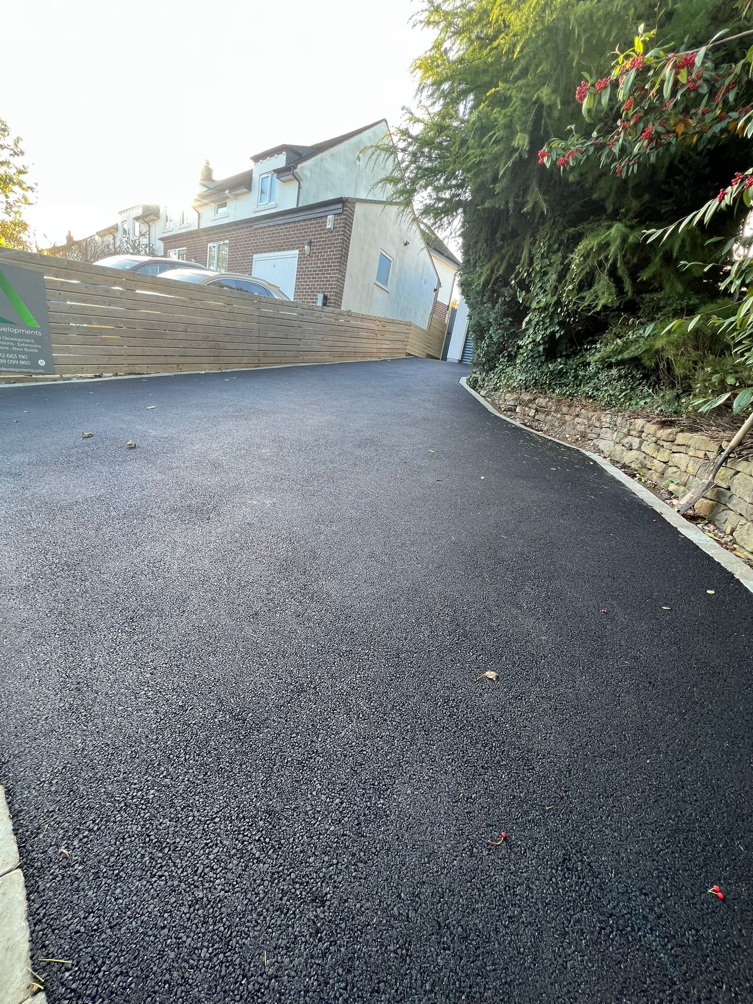 Freshly paved driveway leading to a house, with stone wall and greenery on the side.