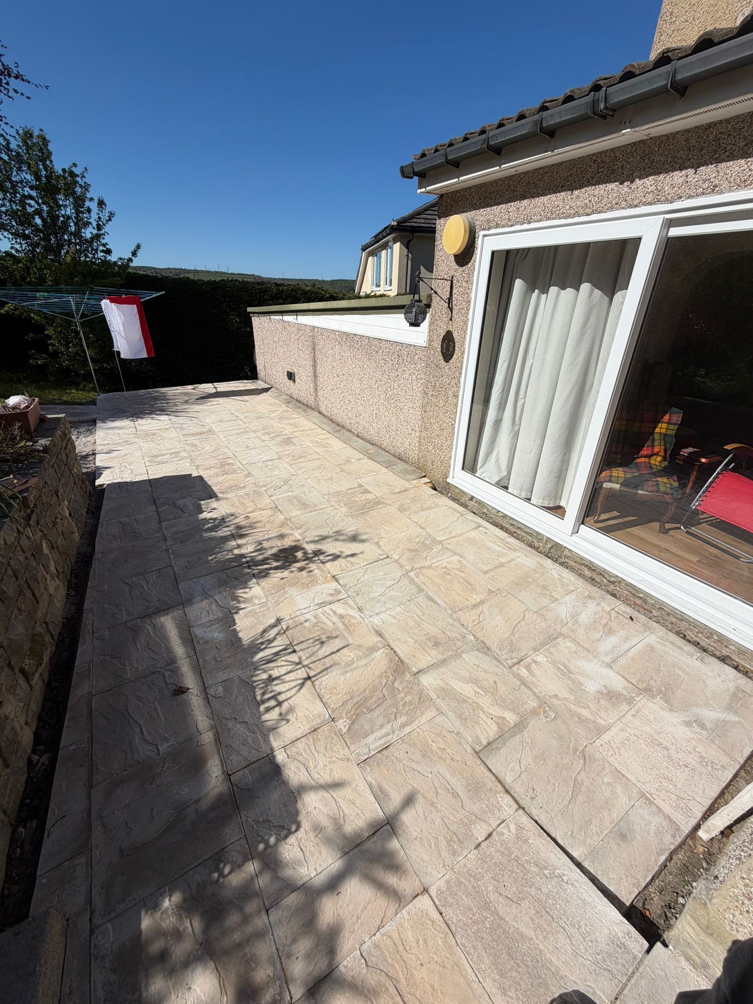 Stone patio beside a house with sliding glass doors, white fence, and blue sky.