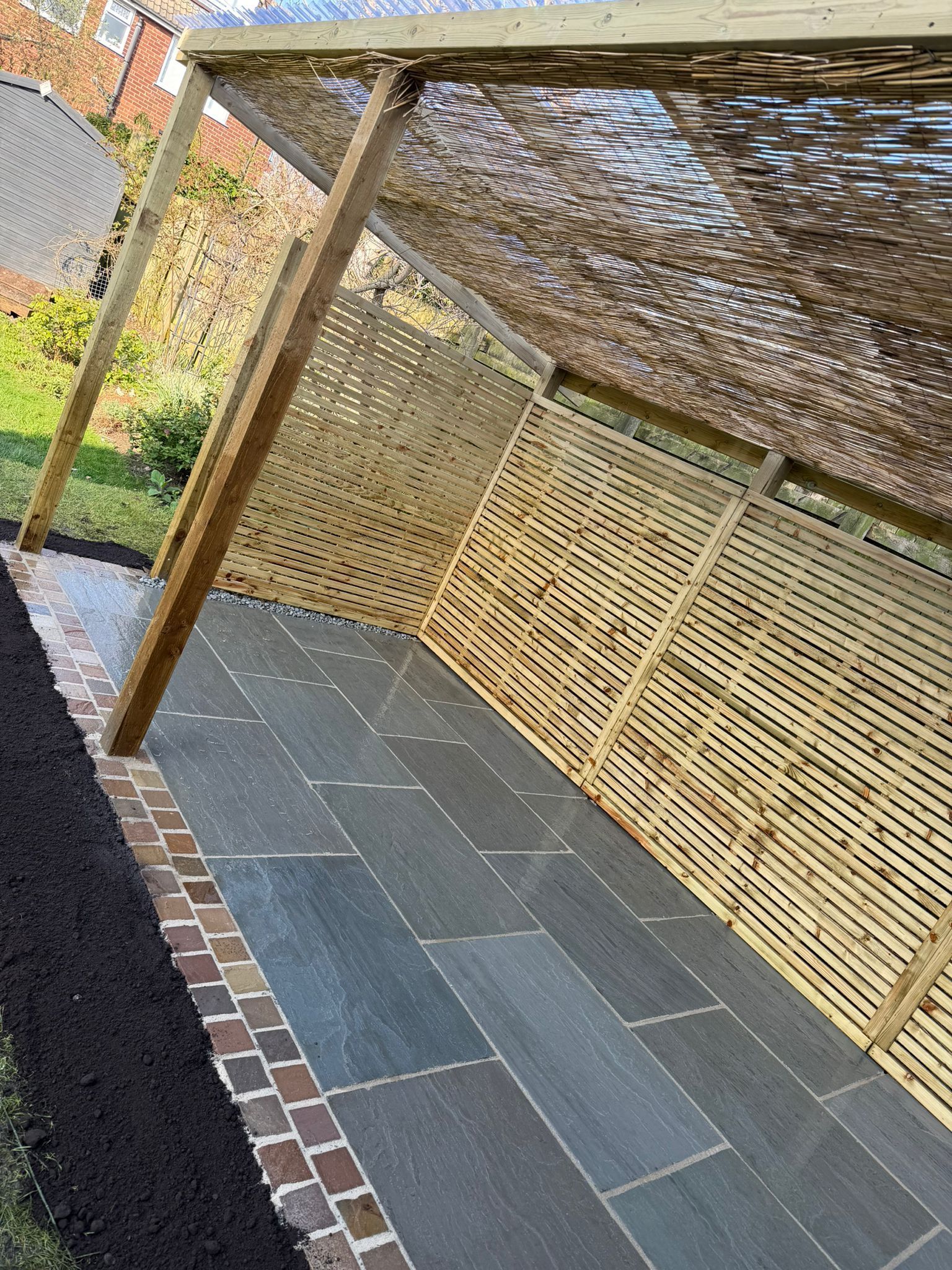 Covered outdoor patio with tiled floor, wooden posts, and woven bamboo screen walls.