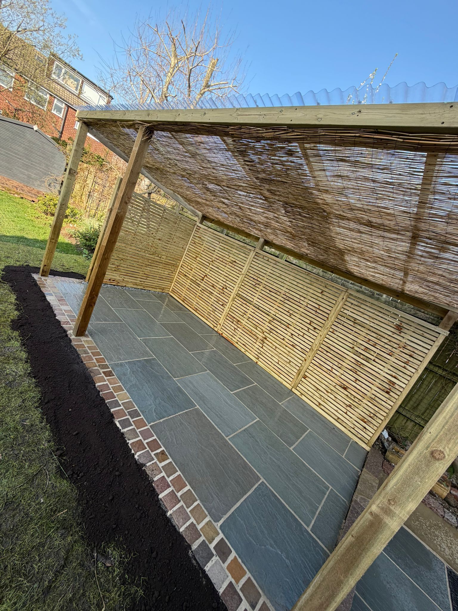 Outdoor patio with a wooden pergola, lattice shade panels, and a stone tile floor beside a brick border.