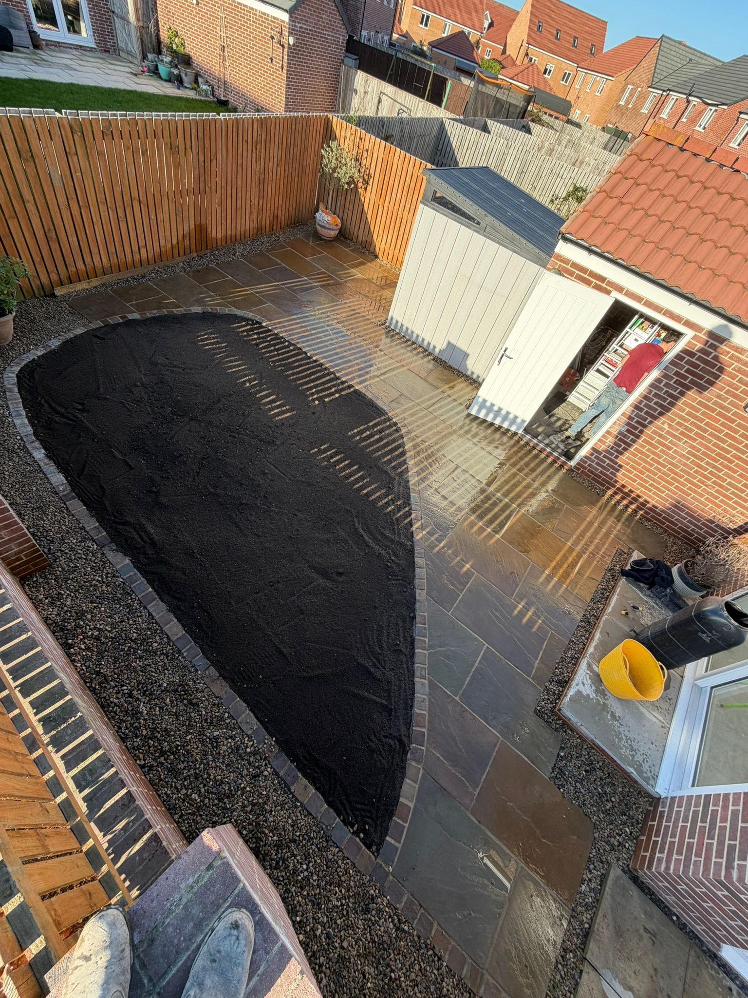 Backyard with a large covered excavation hole, brick walls, and a yellow bucket beside a house
