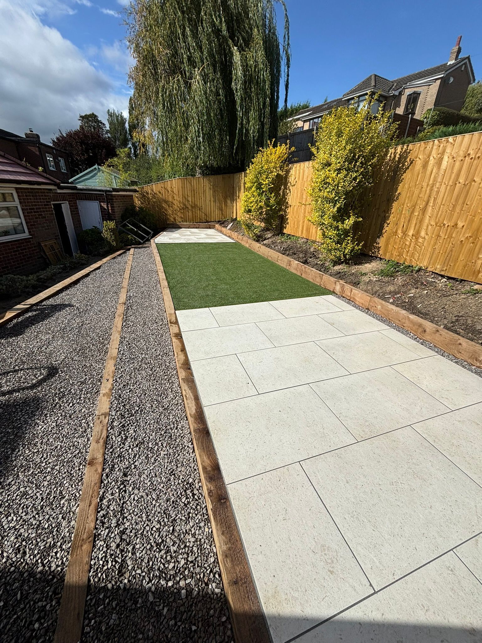 Backyard garden path with concrete slabs, gravel border, and green lawn under bright sunlight