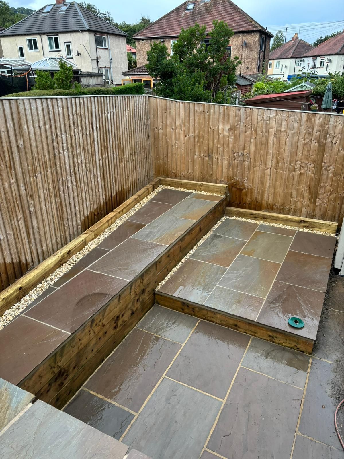 Raised stone patio and steps in a small fenced backyard with bamboo screening.
