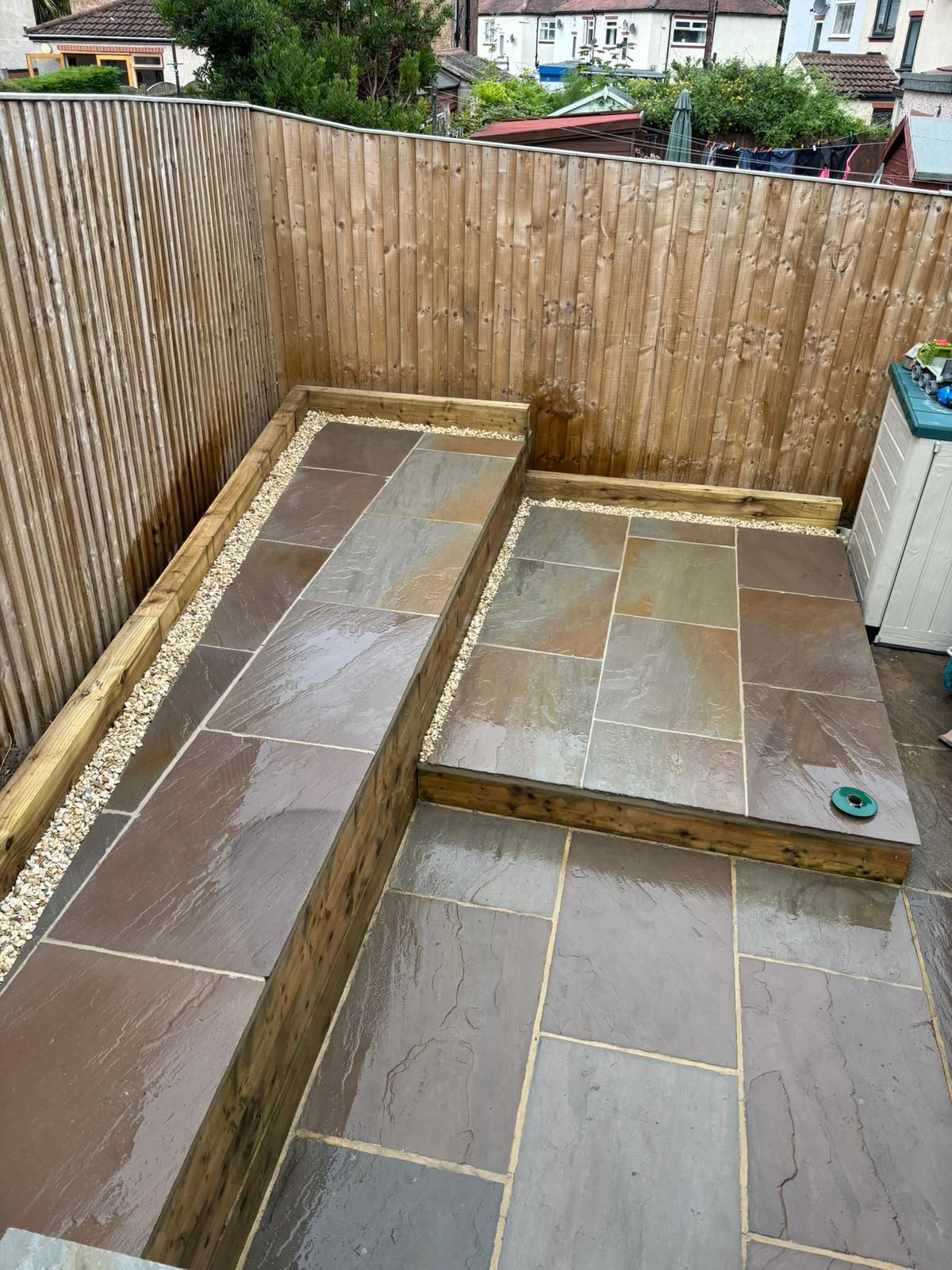 Small paved backyard with raised stone platforms and bamboo fence walls.