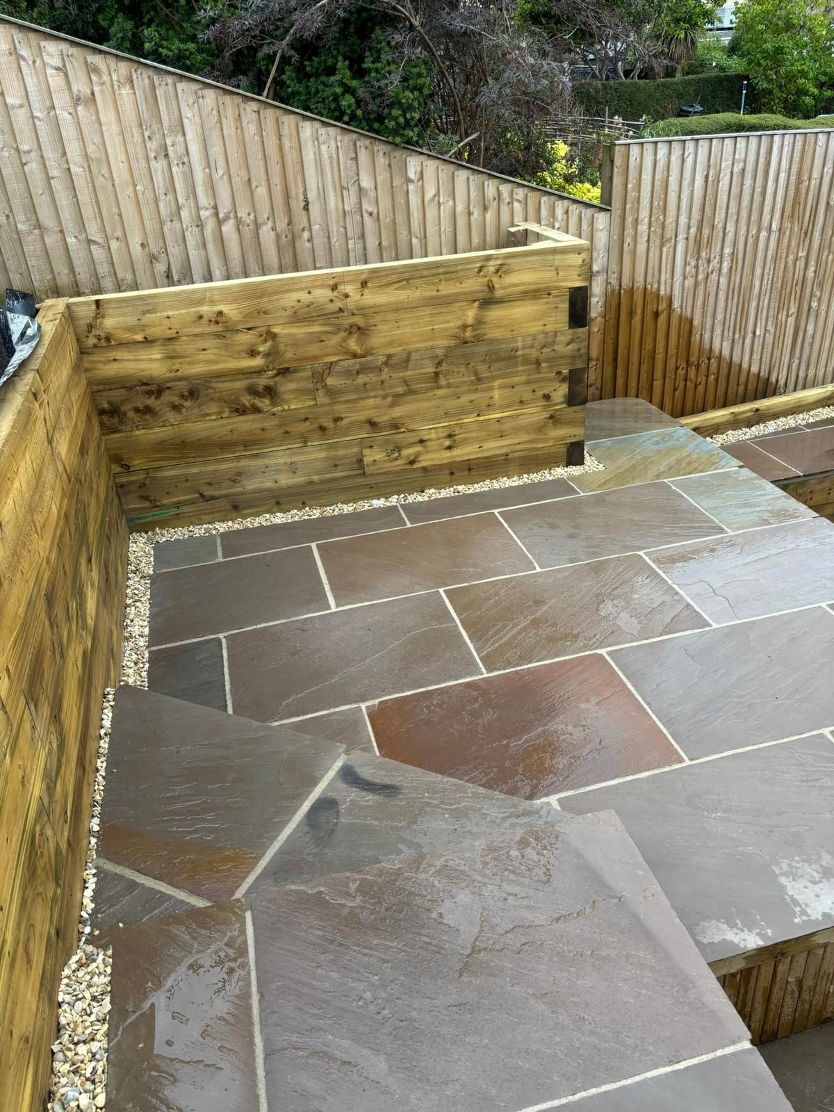 Stone patio with wooden retaining walls on a sloped outdoor terrace.