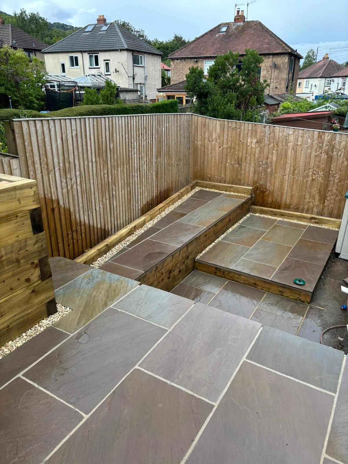 Small paved backyard with wooden fencing, raised planter beds, and houses visible beyond the fence.