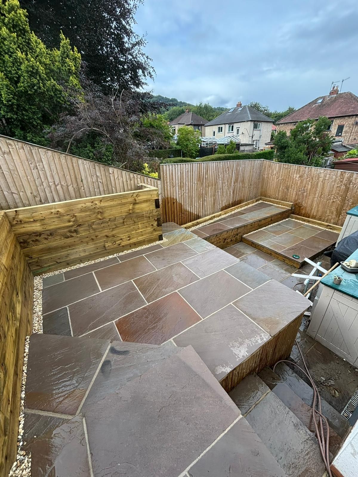 Backyard patio with large stone slabs, raised steps, and wooden fencing, viewed from above