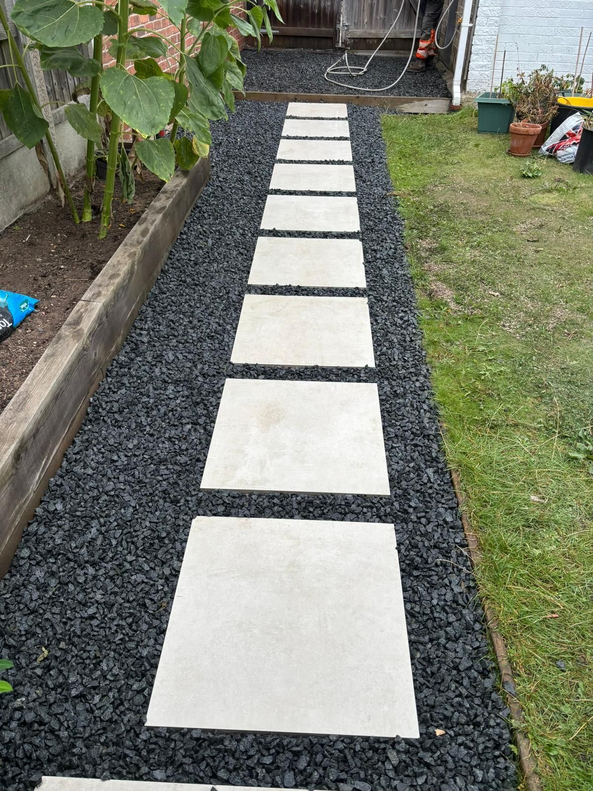 Stepping stone path of white pavers on black gravel leading through a yard to a patio