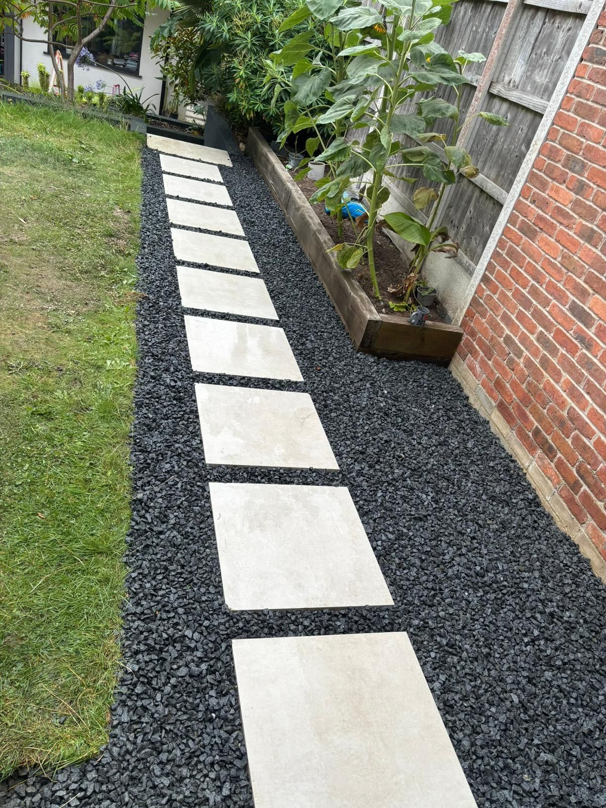 Stepping-stone path of light pavers through black gravel beside a lawn and brick house wall