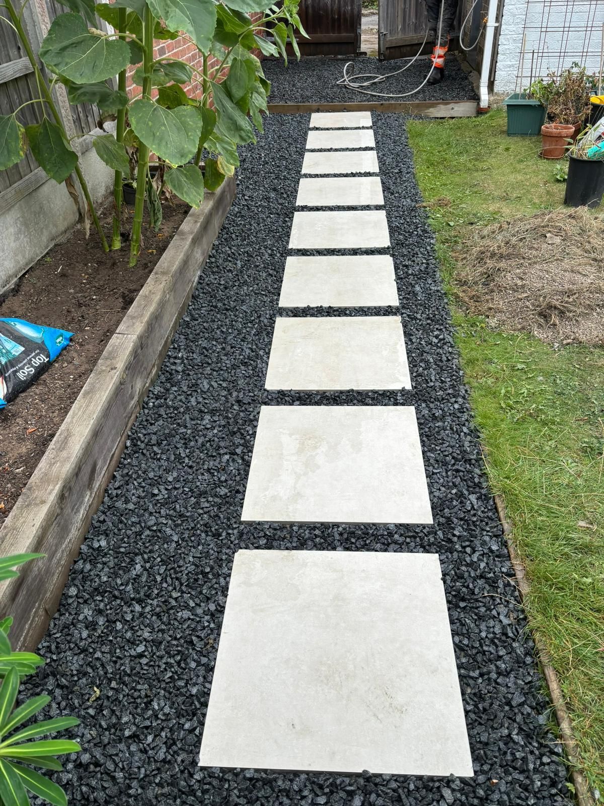 Stepping stone path of white pavers through black gravel beside a grassy yard and plants