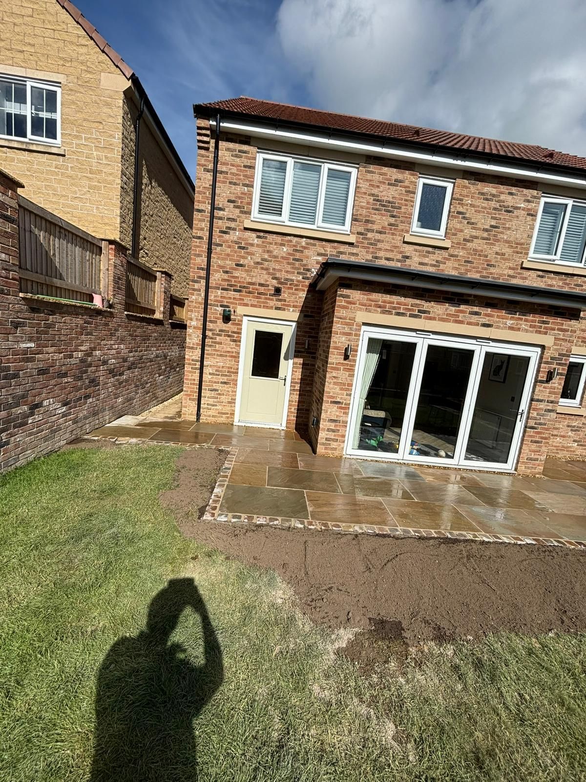 Brick house with patio doors, small lawn, and a shadow in the foreground under a cloudy sky