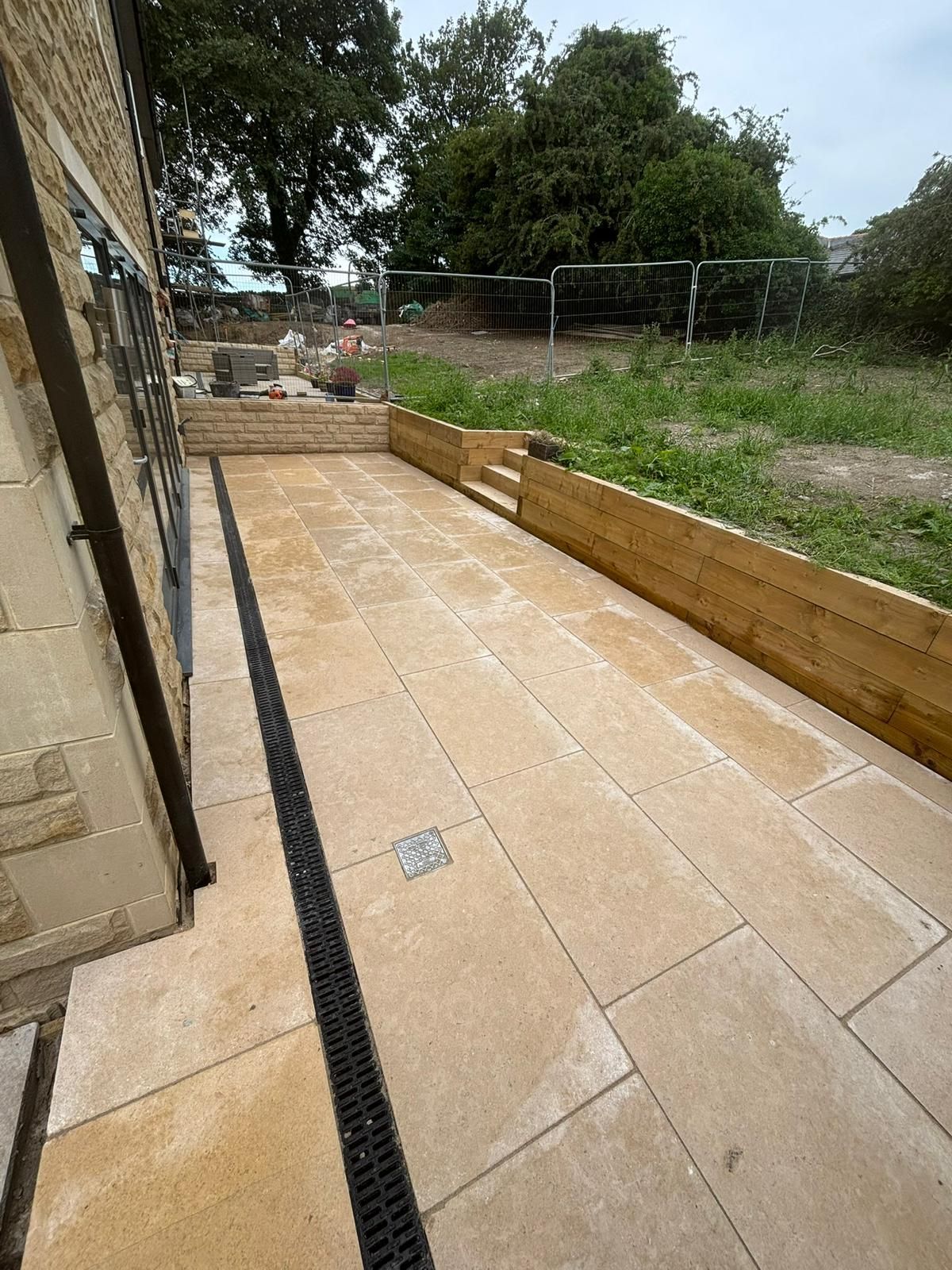 Stone patio beside house with wooden retaining walls and a grassy yard beyond