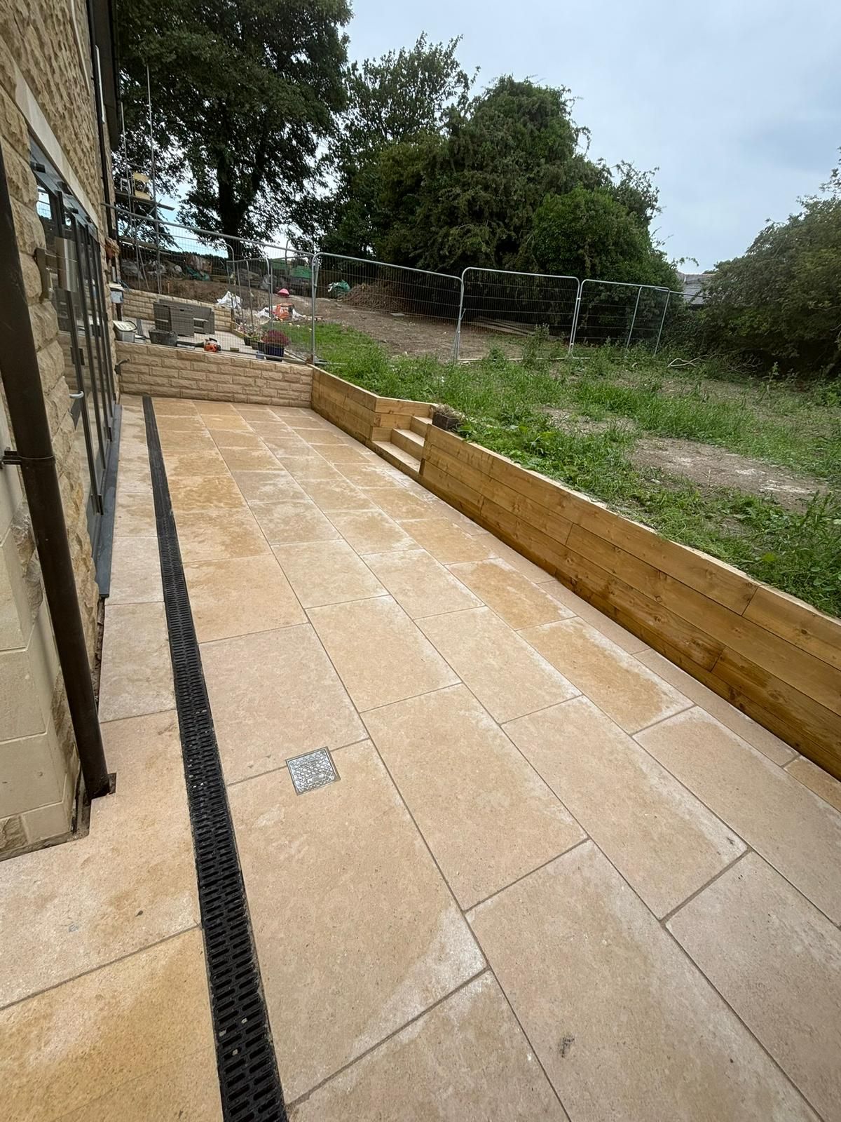 Stone patio beside a house with timber edging and a grassy garden beyond