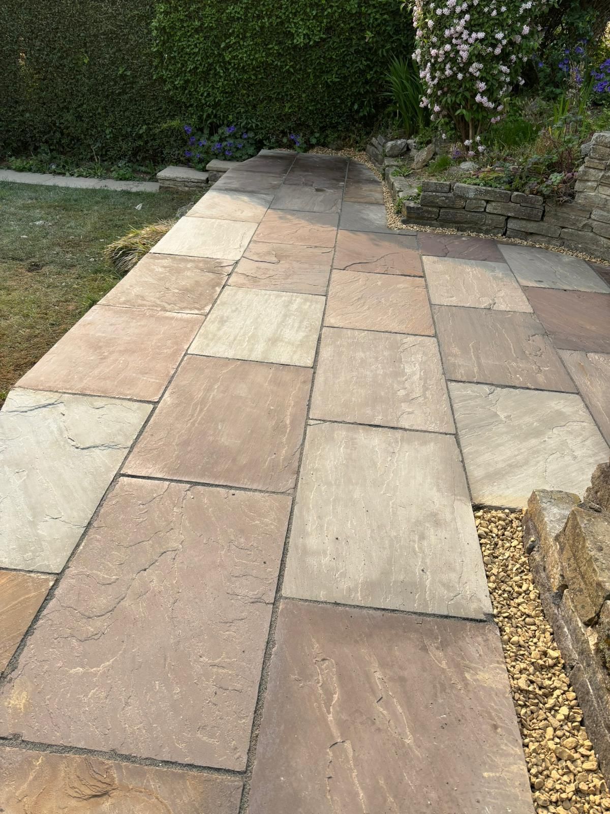 Stone garden path leading through a hedge-lined walkway with beige and pink paving slabs