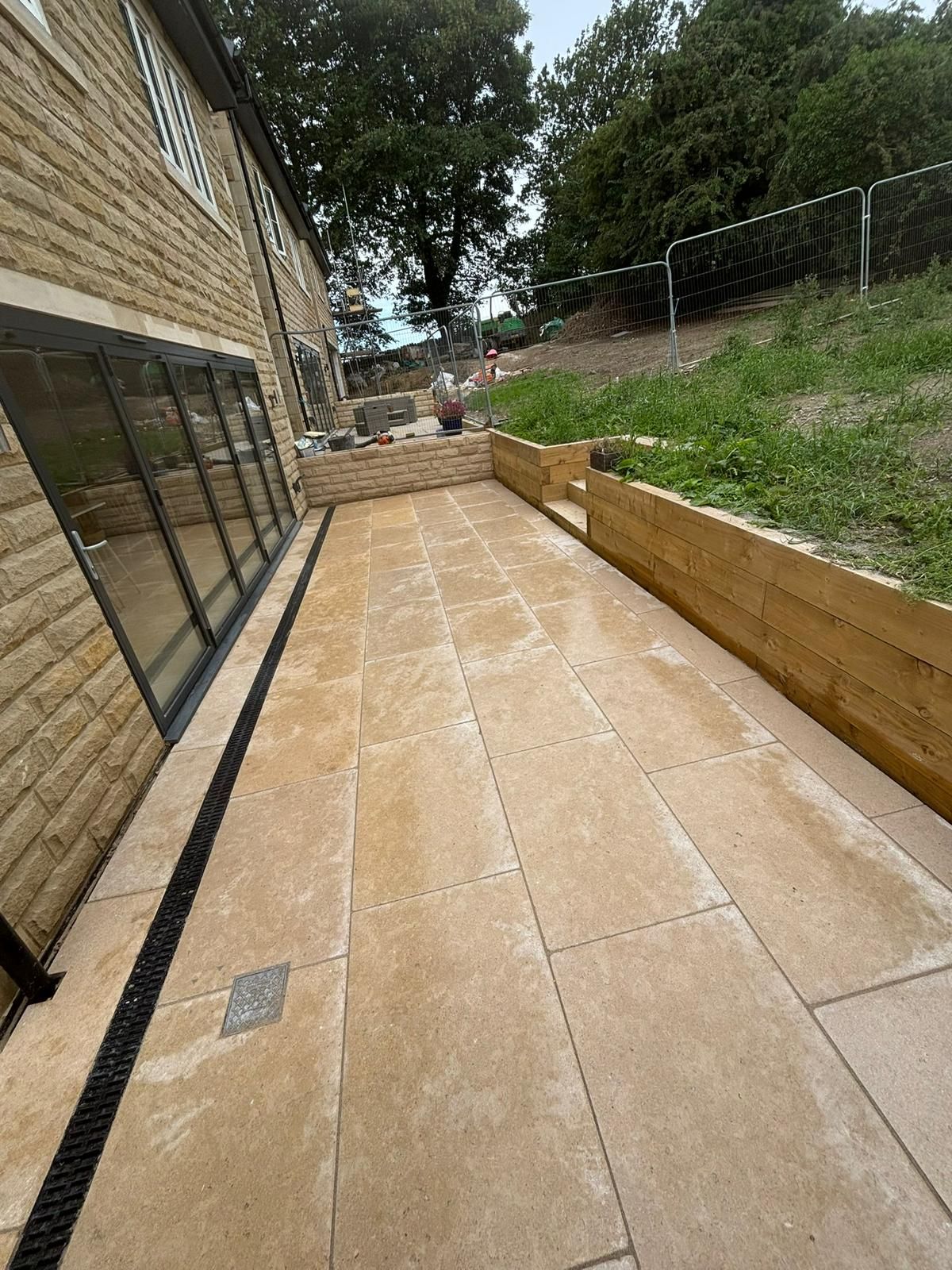 Outdoor stone walkway beside a brick building, with a grassy slope and trees along the right side.