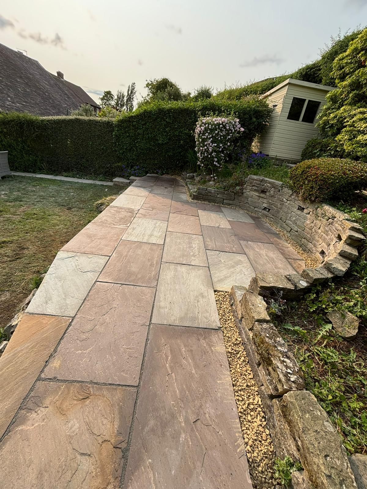 Stone garden path beside a hedge and gravel edge, leading toward a small white building.