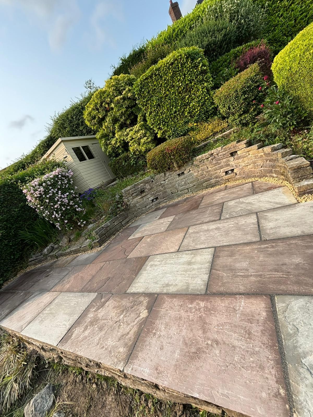 Stone patio beside trimmed hedges and a small garden shed on a sunny day
