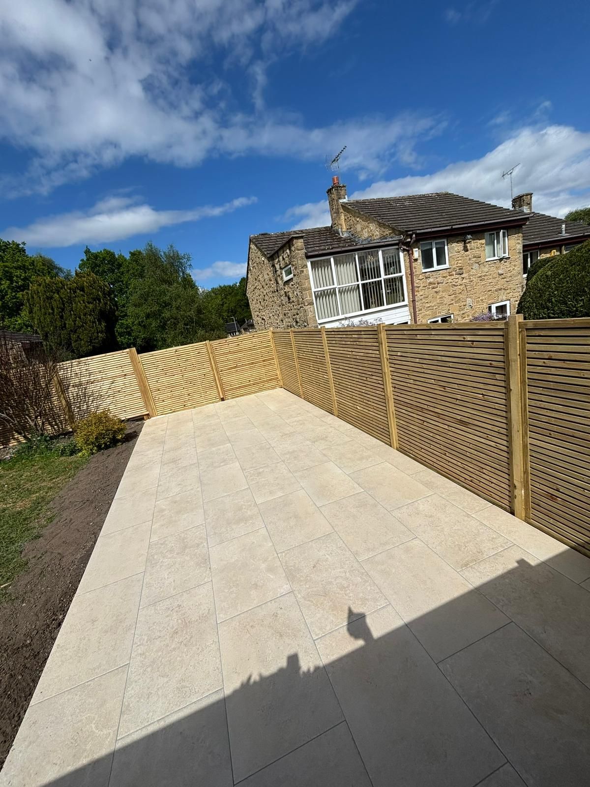 Stone-paved driveway leading to a rustic house with a wooden fence under a blue sky.