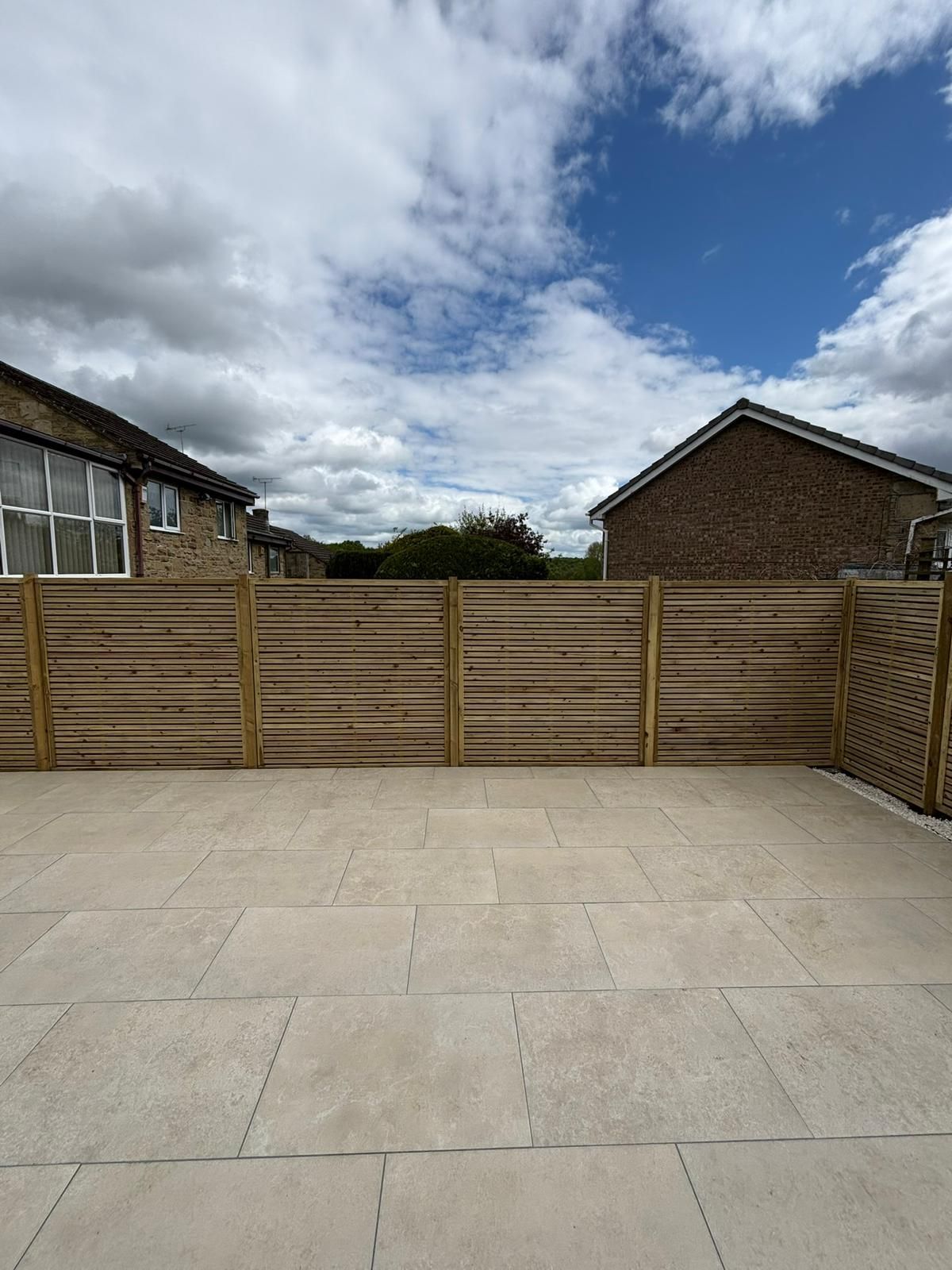 Stone patio facing a wooden fence between houses under a cloudy sky